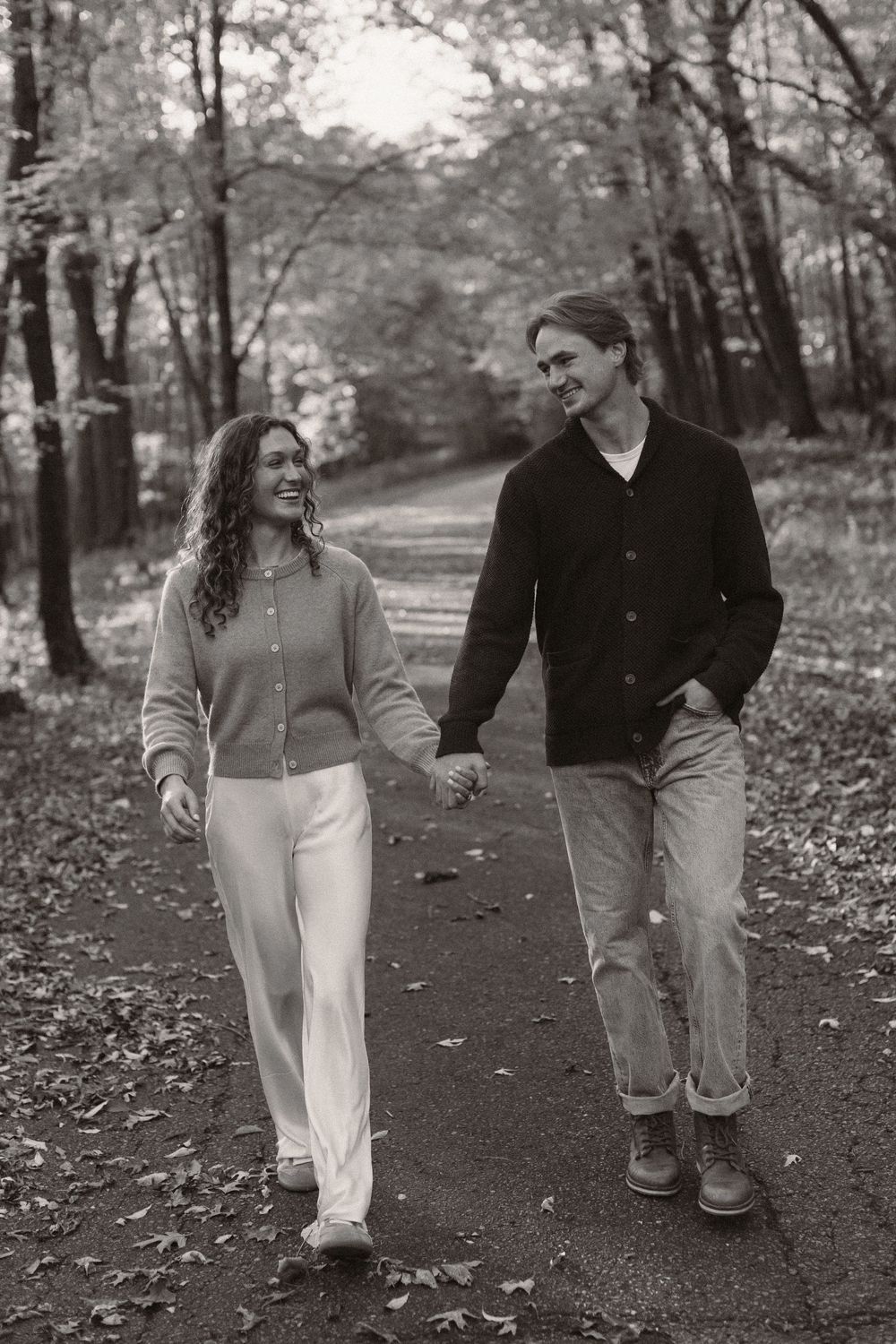 A couple walking hand in hand along a wooded path in black and white.