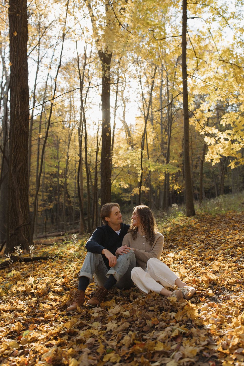 A romantic autumn scene of a couple sitting together on fallen leaves in a sunlit forest.