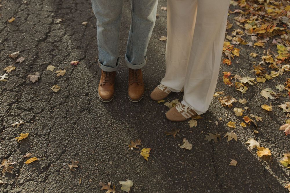 Two pairs of feet in casual shoes standing on a path covered with autumn leaves.