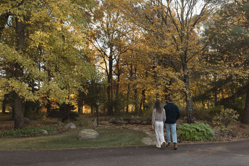A couple walking together on a path surrounded by golden autumn trees at sunset.