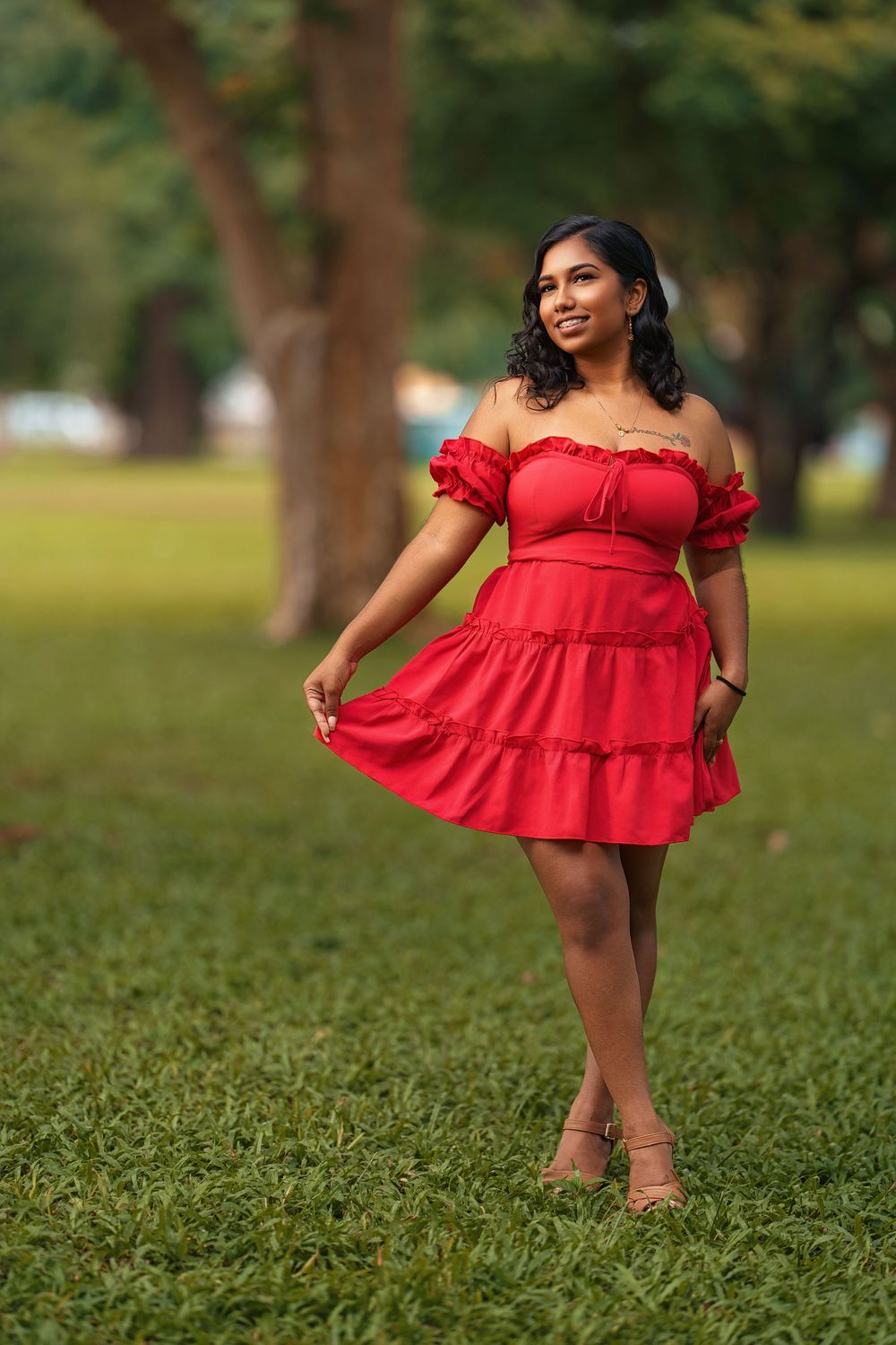 A bright red summer dress with ruffled details is displayed in an outdoor park setting.