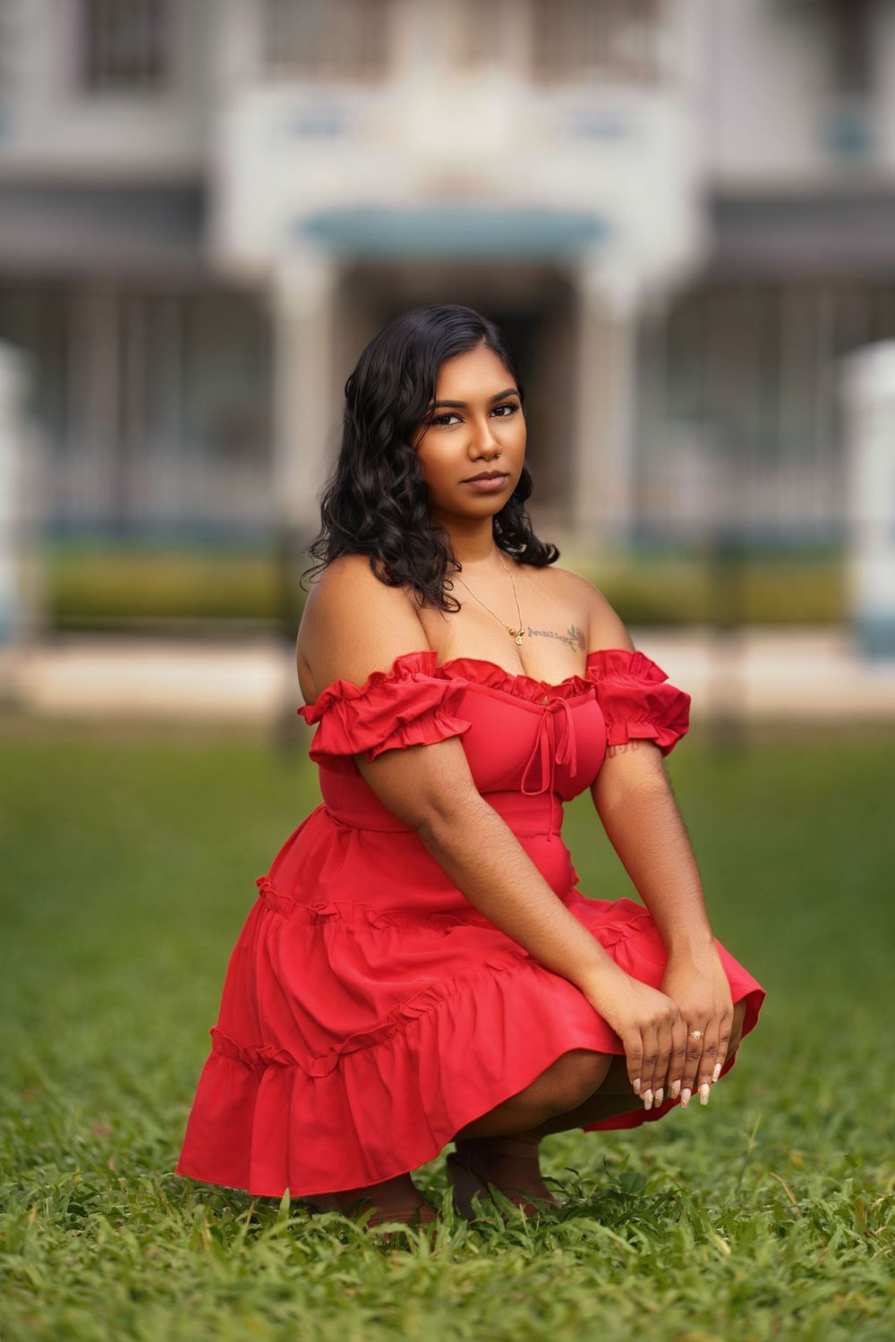 A person in a vibrant red off-shoulder dress sits gracefully on lush green grass in an outdoor setting.