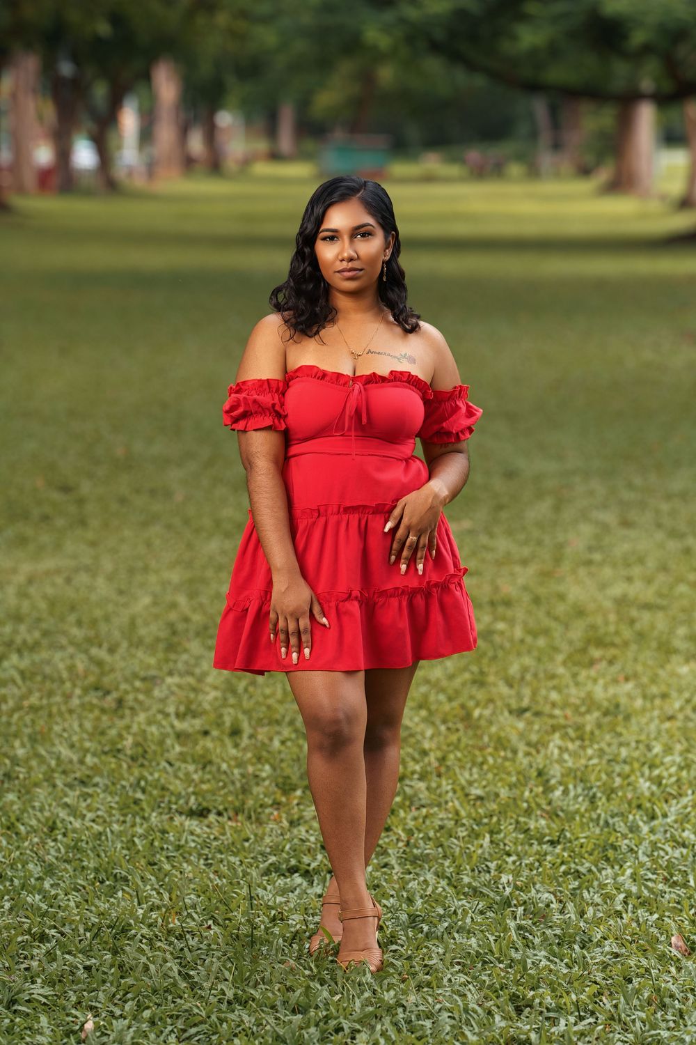 A red off-shoulder ruffle dress is showcased against a lush green lawn background on a sunny day.