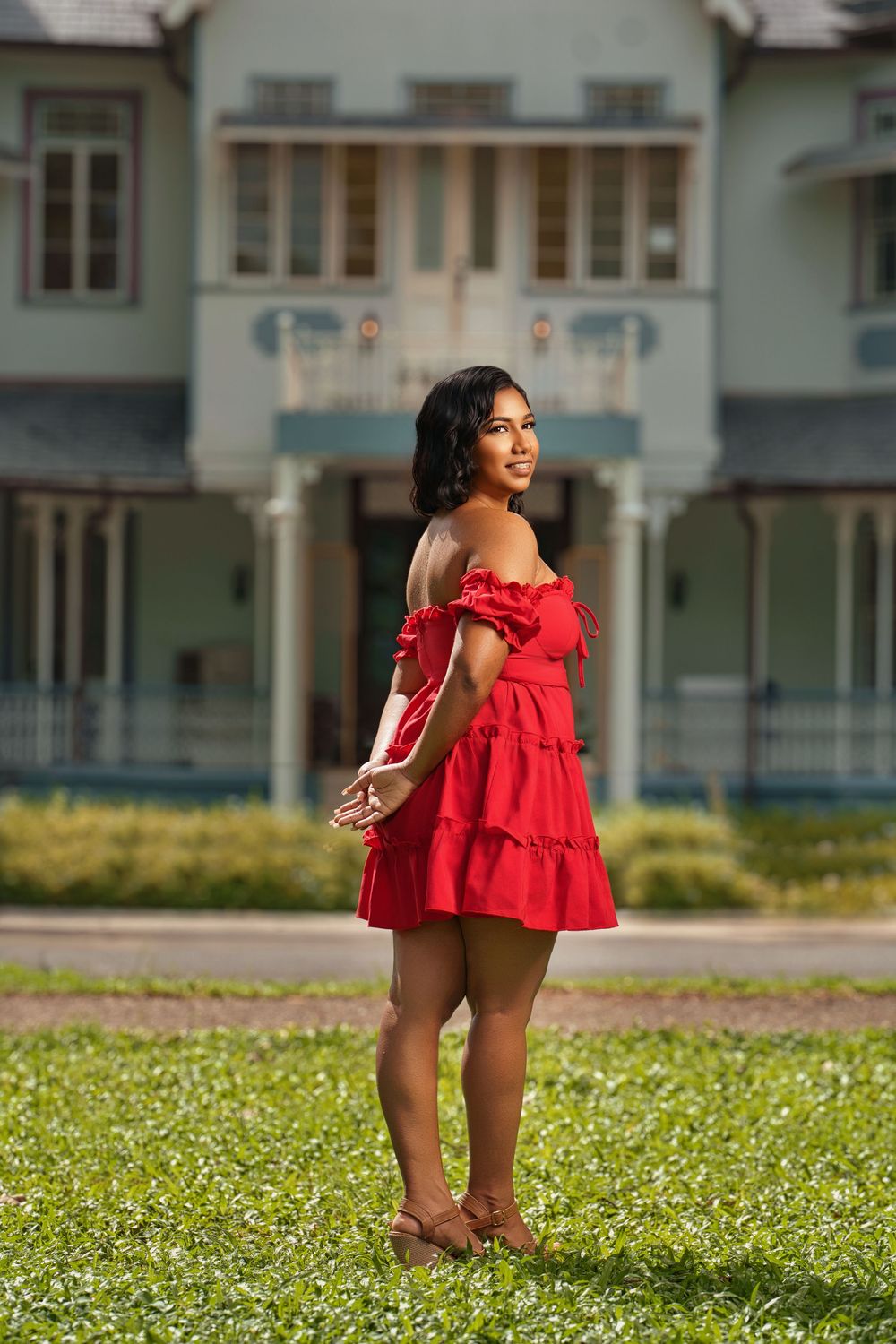 A vibrant red dress with ruffle details is photographed in front of a residential building.