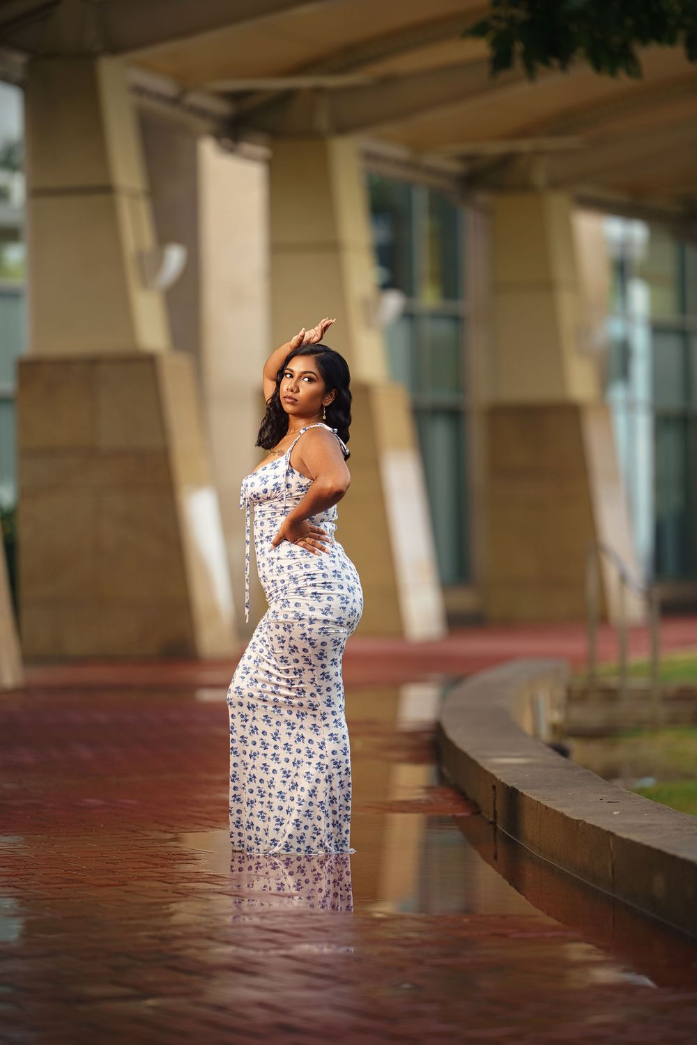 A floral sundress is showcased in an outdoor photoshoot under architectural columns with warm lighting.