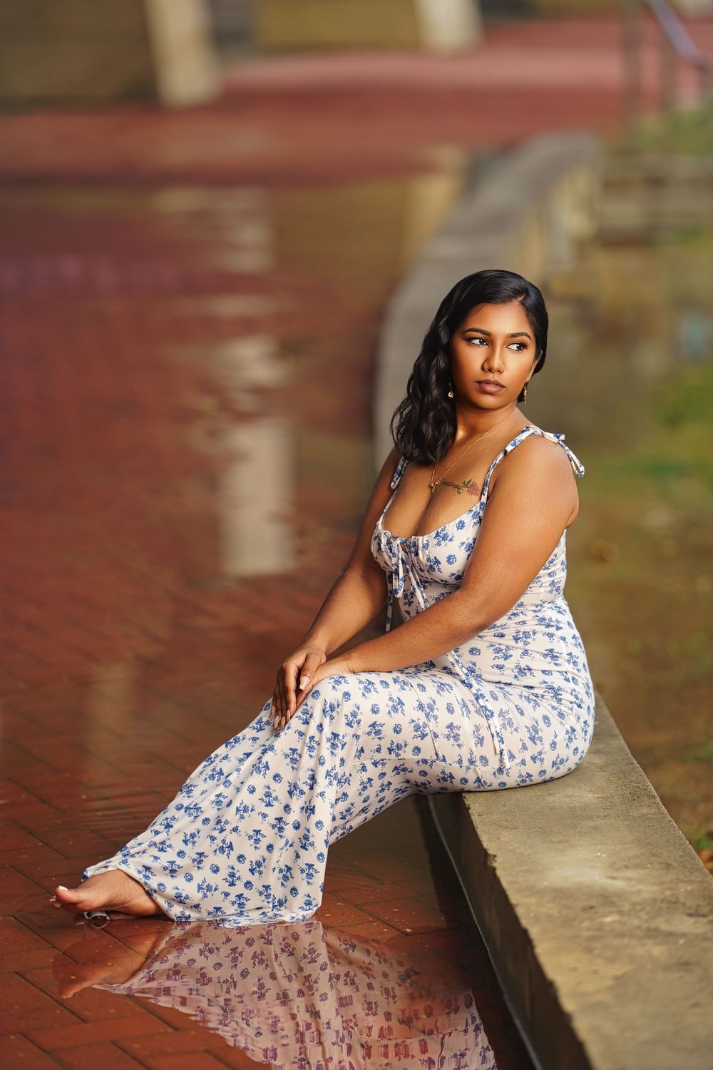 Woman in floral print maxi dress poses elegantly on brick ledge during golden hour photoshoot.