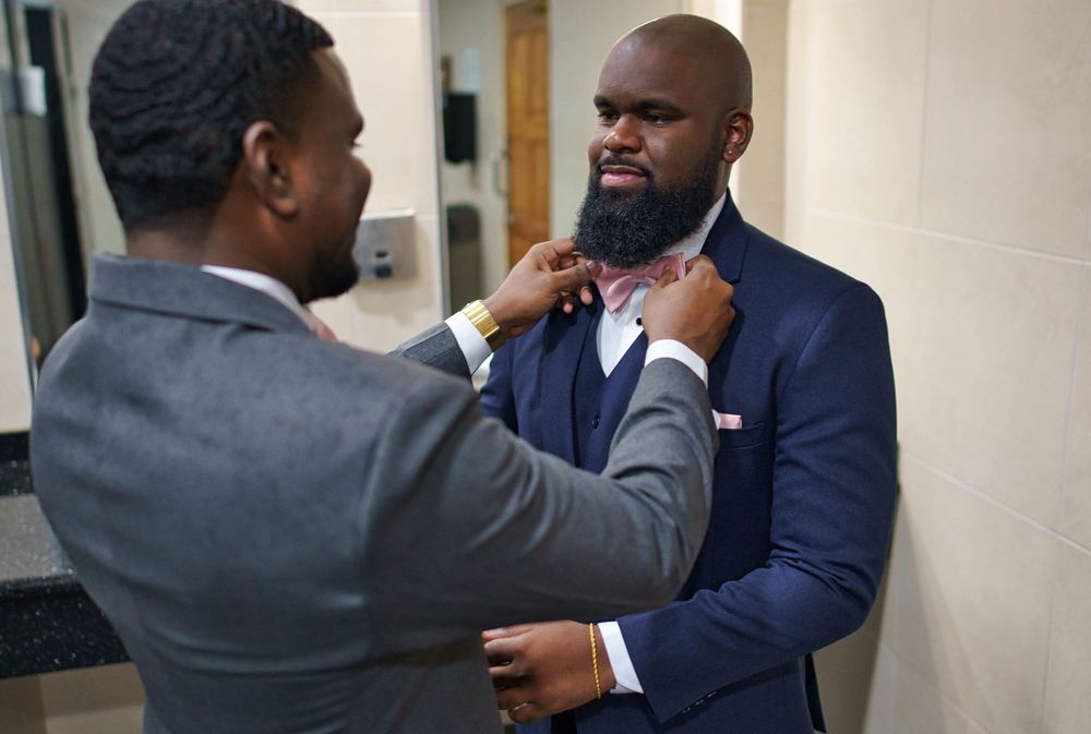 Two people in business attire shake hands in a professional office hallway setting.