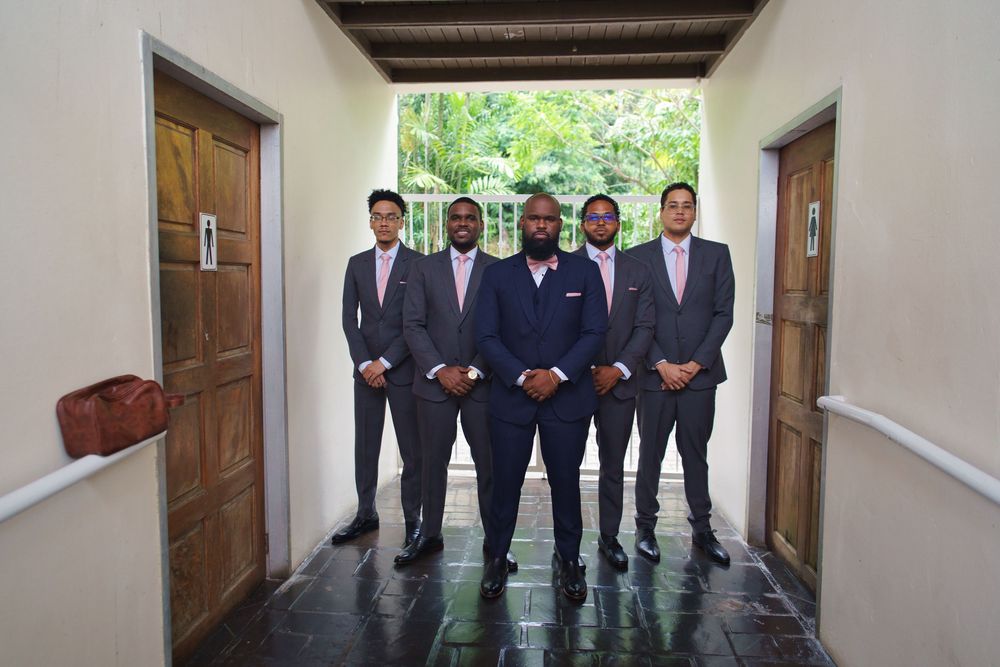 Groomsmen in matching navy suits pose together in a hallway before a wedding ceremony.