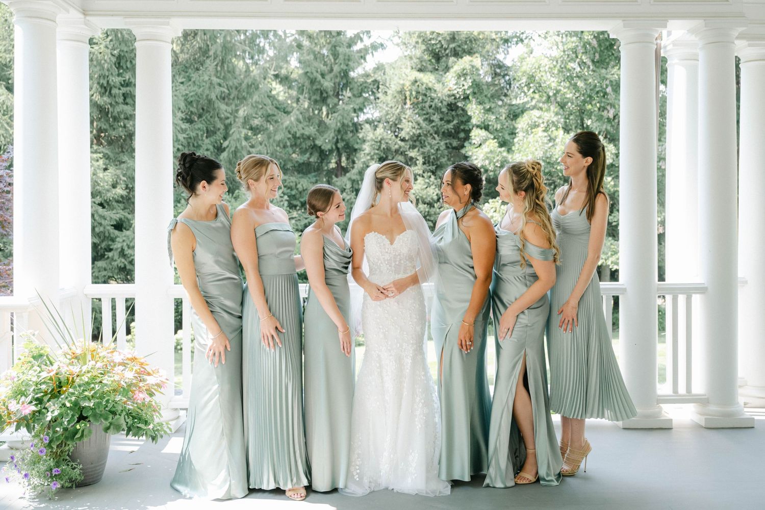 Wedding party in sage green bridesmaid dresses poses under white columned gazebo during outdoor ceremony. - Lake Forest