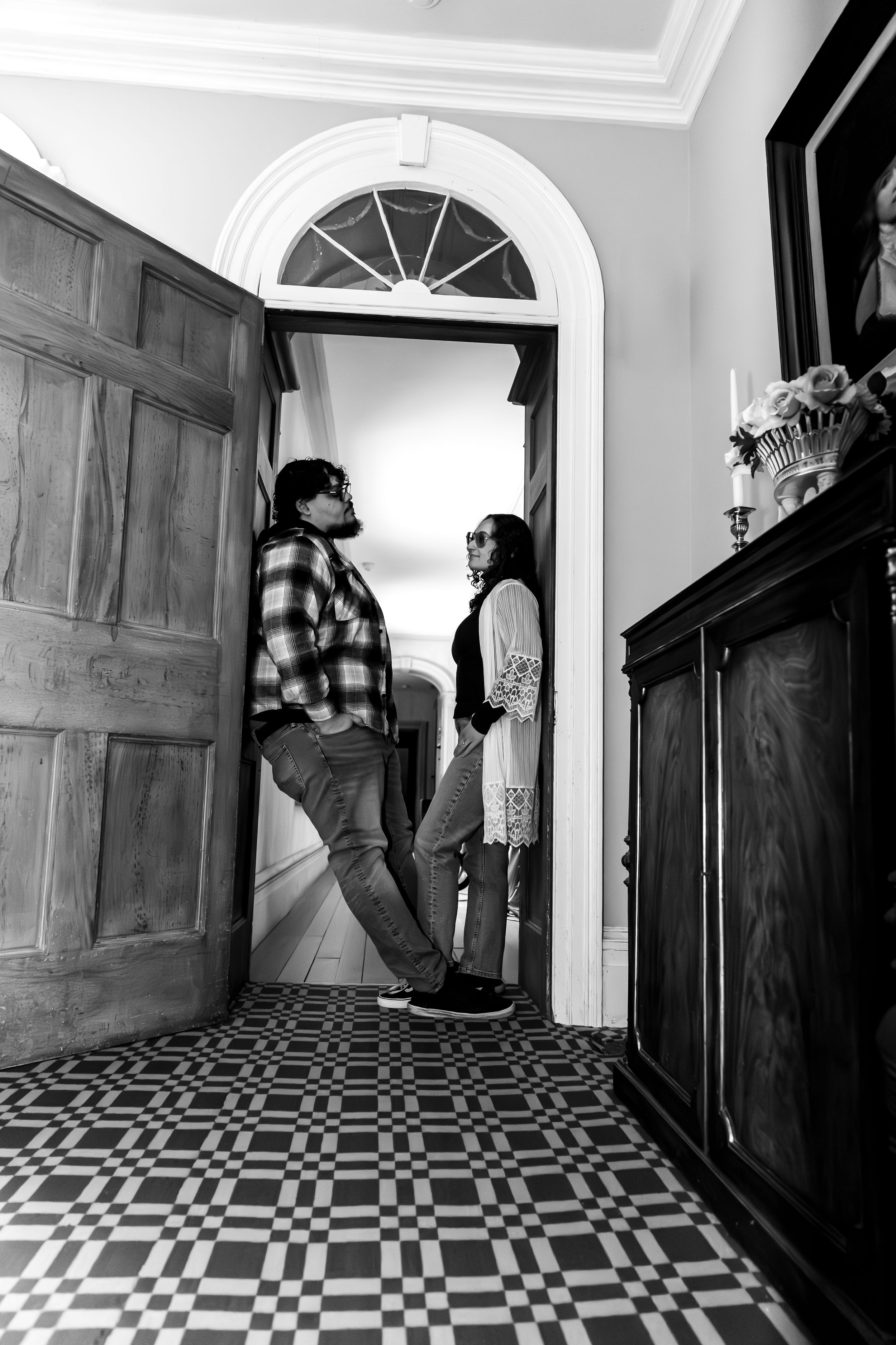 Black and white photo of a couple standing in an elegant doorway with arched transom and checkered floor.