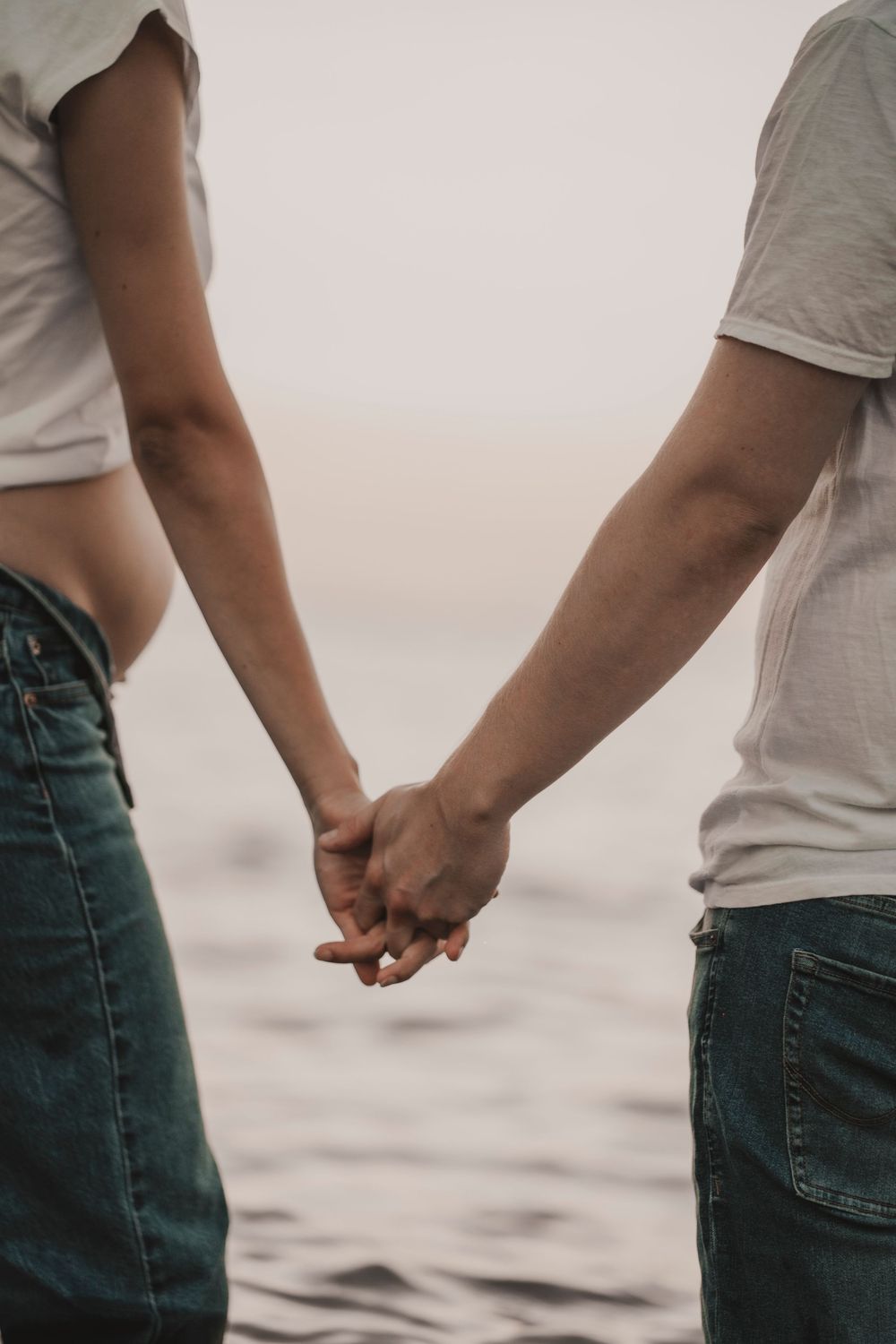 Close up of a couple holding hands with sand blowing gently, cinematic beach shoot vibe.