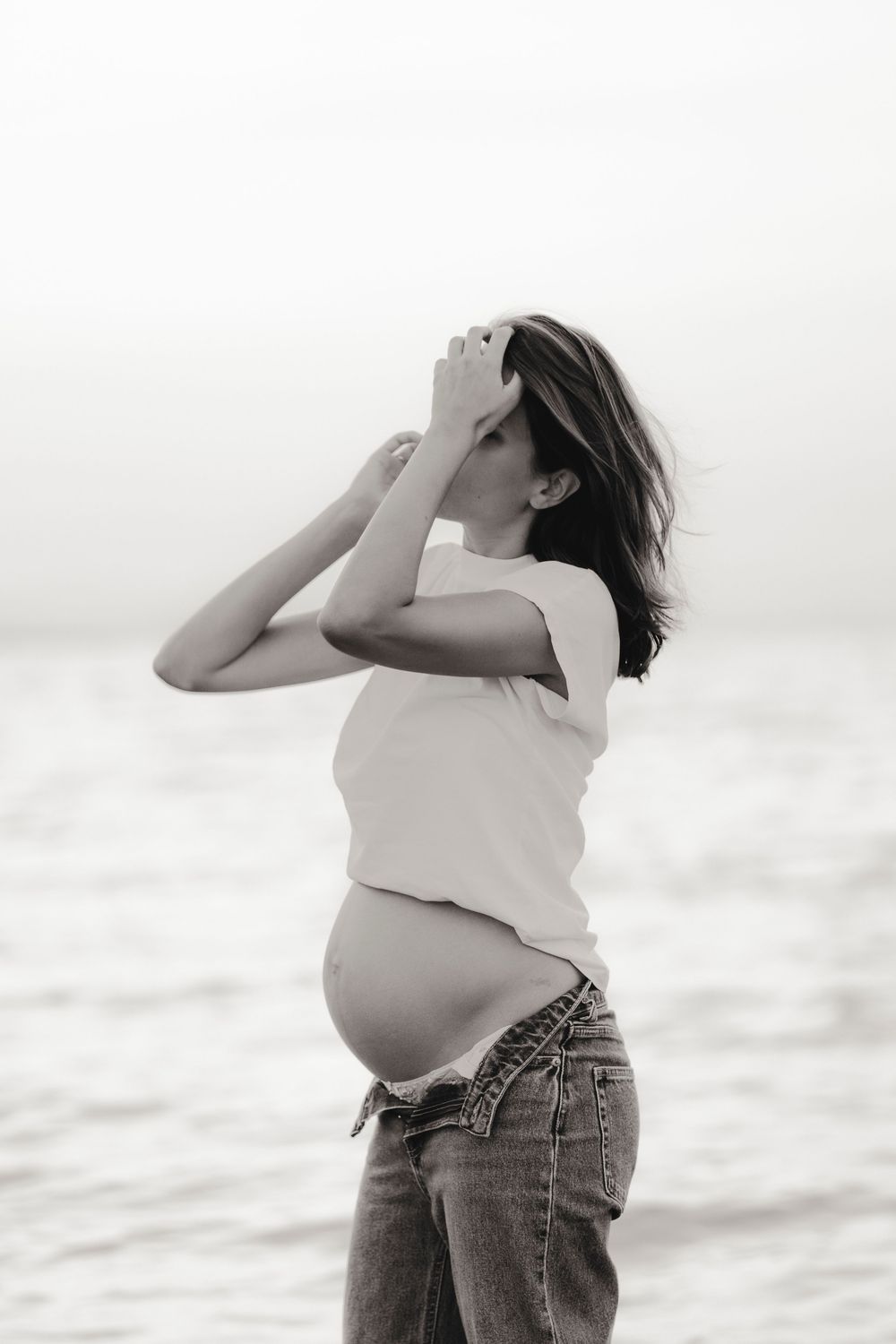 Elegant maternity inspiration with a woman gently holding her baby bump in front of Caorle sea church.