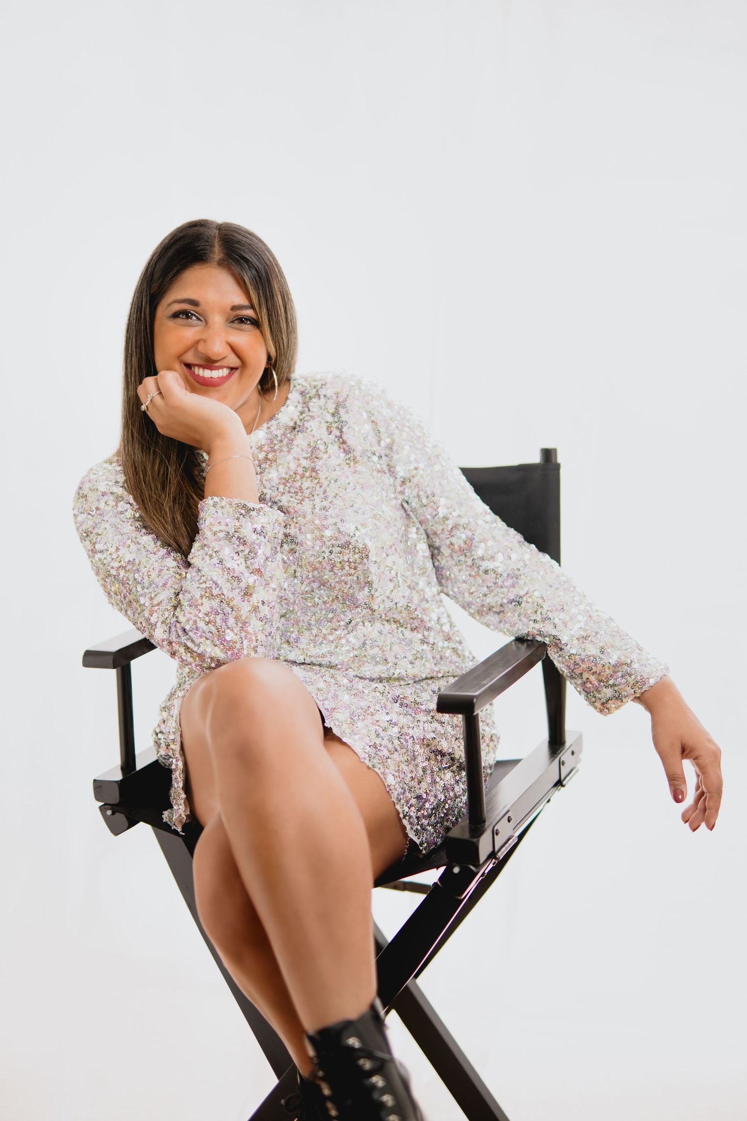 A person in a floral print top poses confidently in a director's chair against a white backdrop.