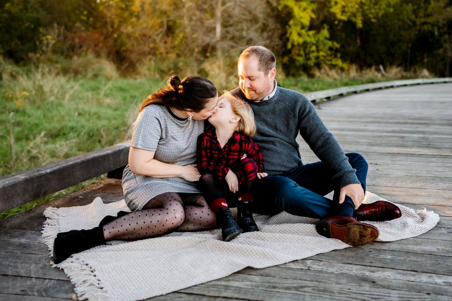 Family sitting together on a blanket on a wooden boardwalk during autumn.