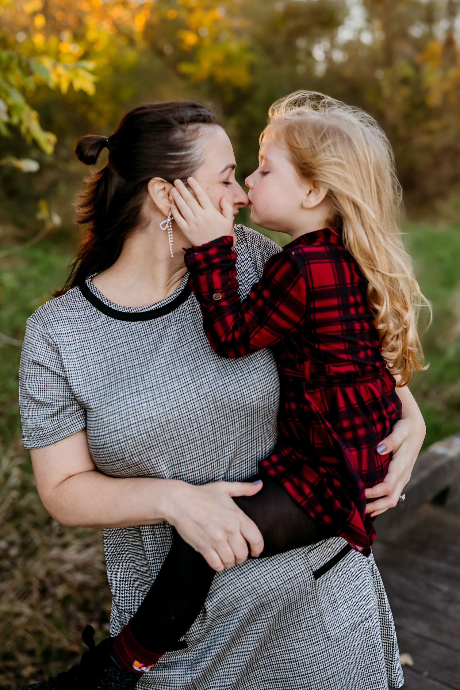 Parent and child in matching plaid sharing a tender moment against fall foliage.