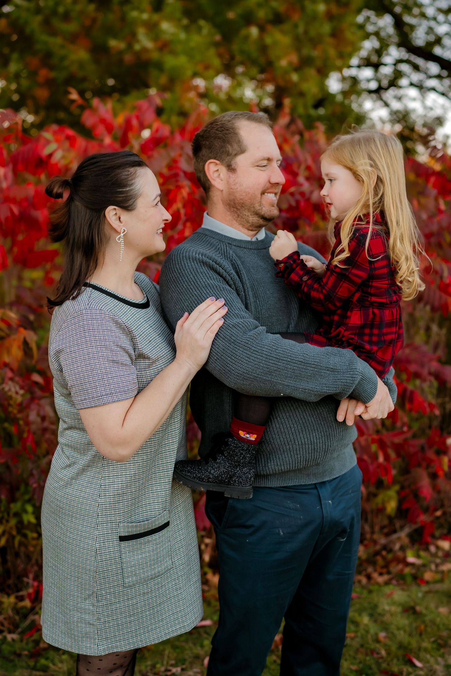A couple embraces in front of vibrant red autumn foliage during a romantic outdoor photo session.