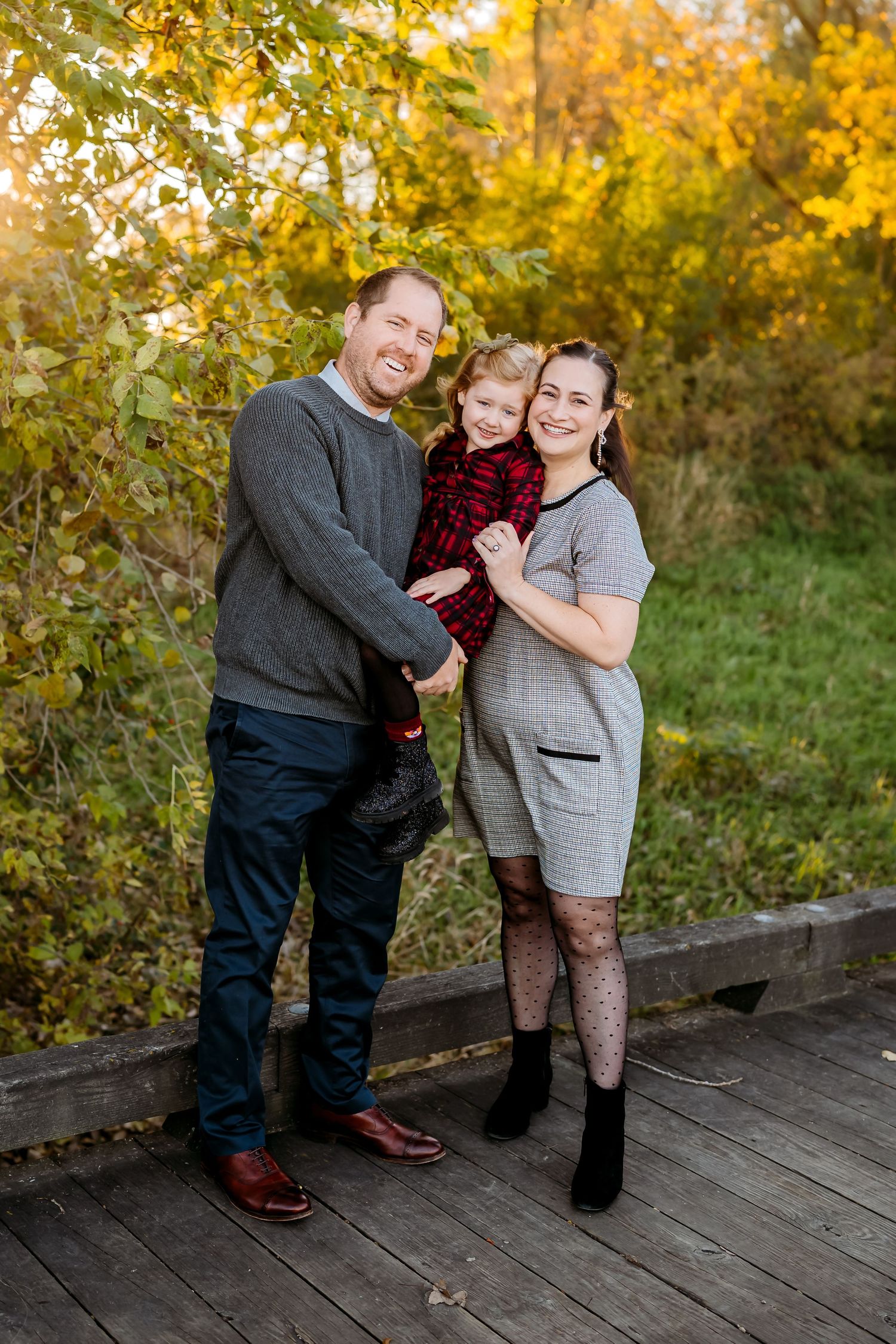 A couple shares a joyful dance moment together on a wooden deck surrounded by autumn foliage at sunset.