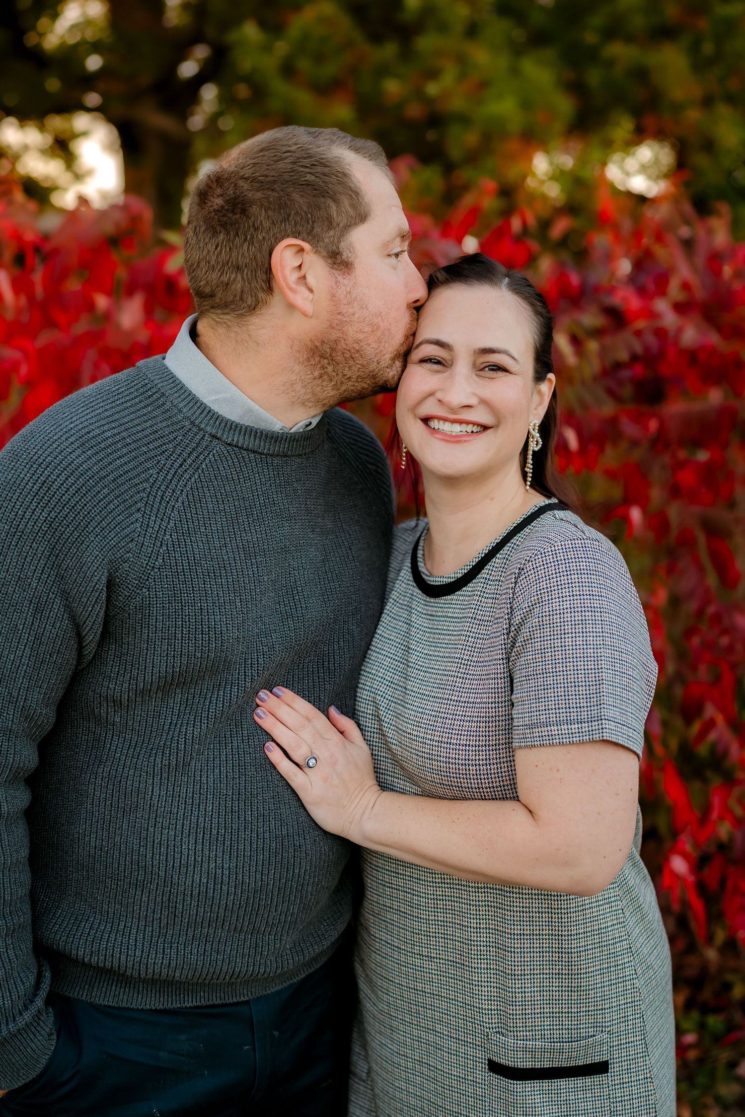 A couple shares a romantic moment in front of vibrant red autumn foliage during an outdoor photo session.