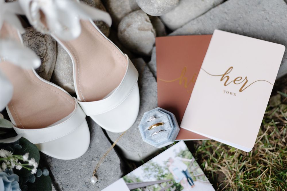White wedding shoes and elegant stationery arranged on grass with delicate floral accents.