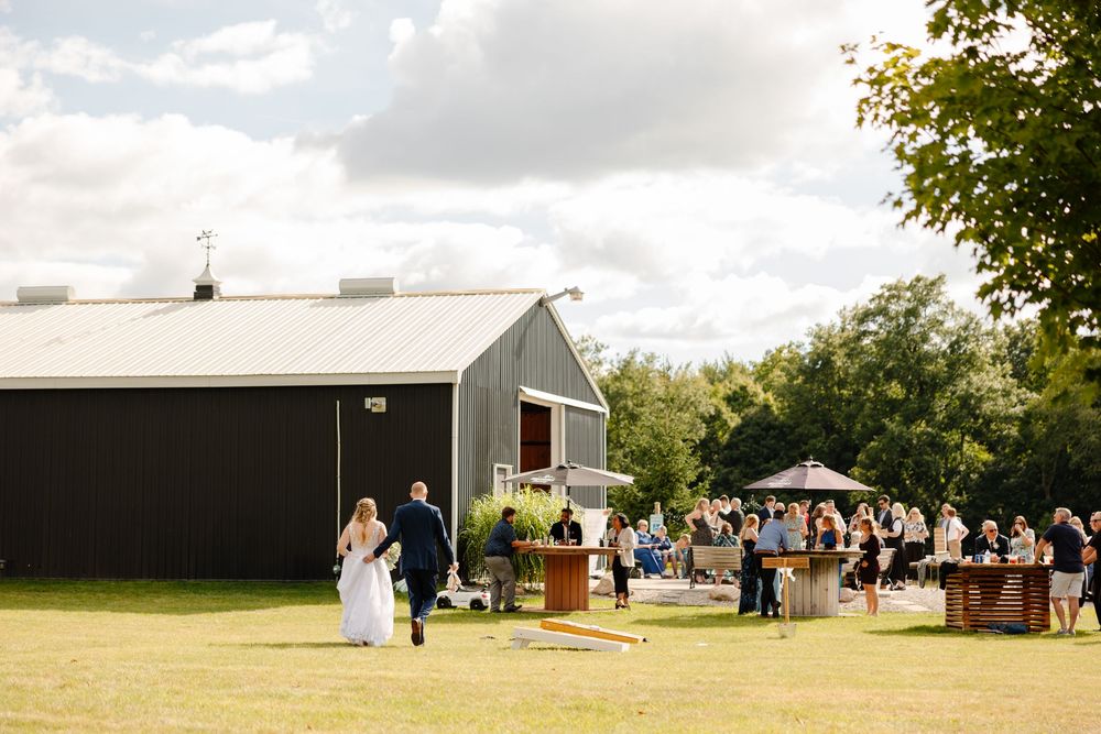 An outdoor wedding ceremony setup with white chairs and guests on a grassy field near a rustic barn.