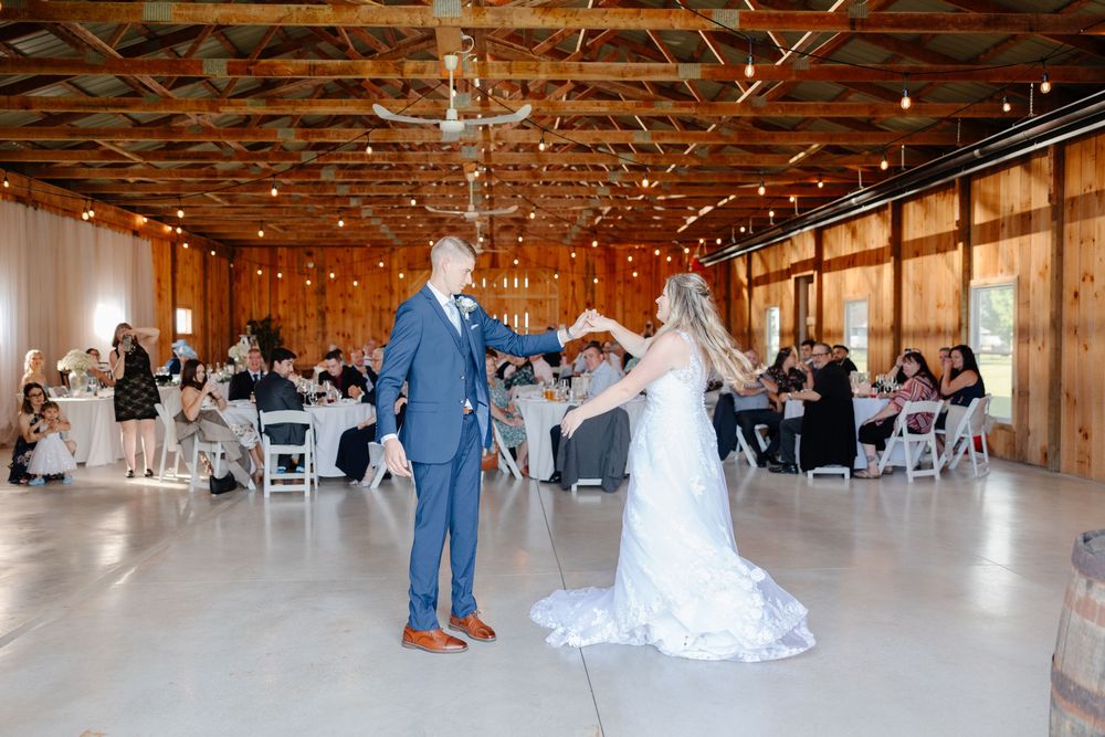 Panoramic view of a rustic barn wedding reception venue with wooden beams and white chairs set up for guests.