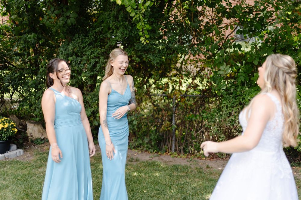 Bridesmaids in light blue dresses pose together in a garden setting during an outdoor wedding celebration.