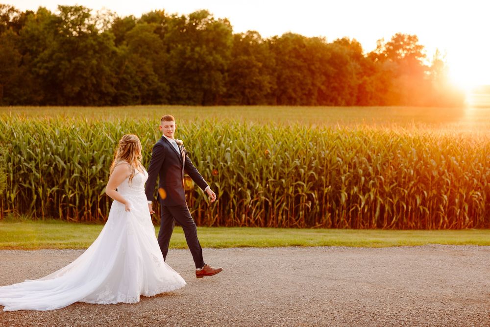 Romantic sunset wedding photo in a golden cornfield with flowing white dress and warm evening light.