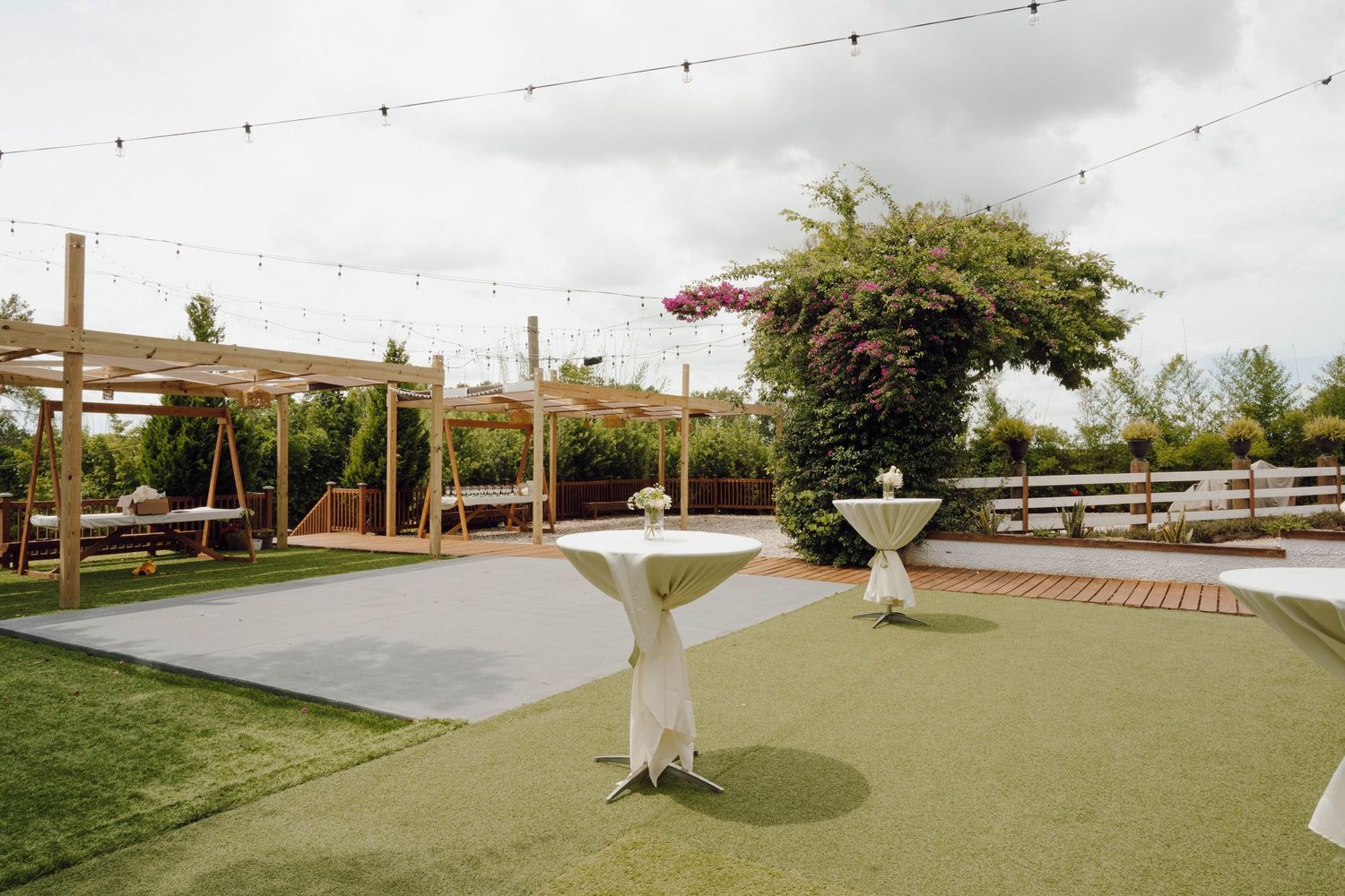 String lights hang over an outdoor wedding reception area with a dance floor and seating.