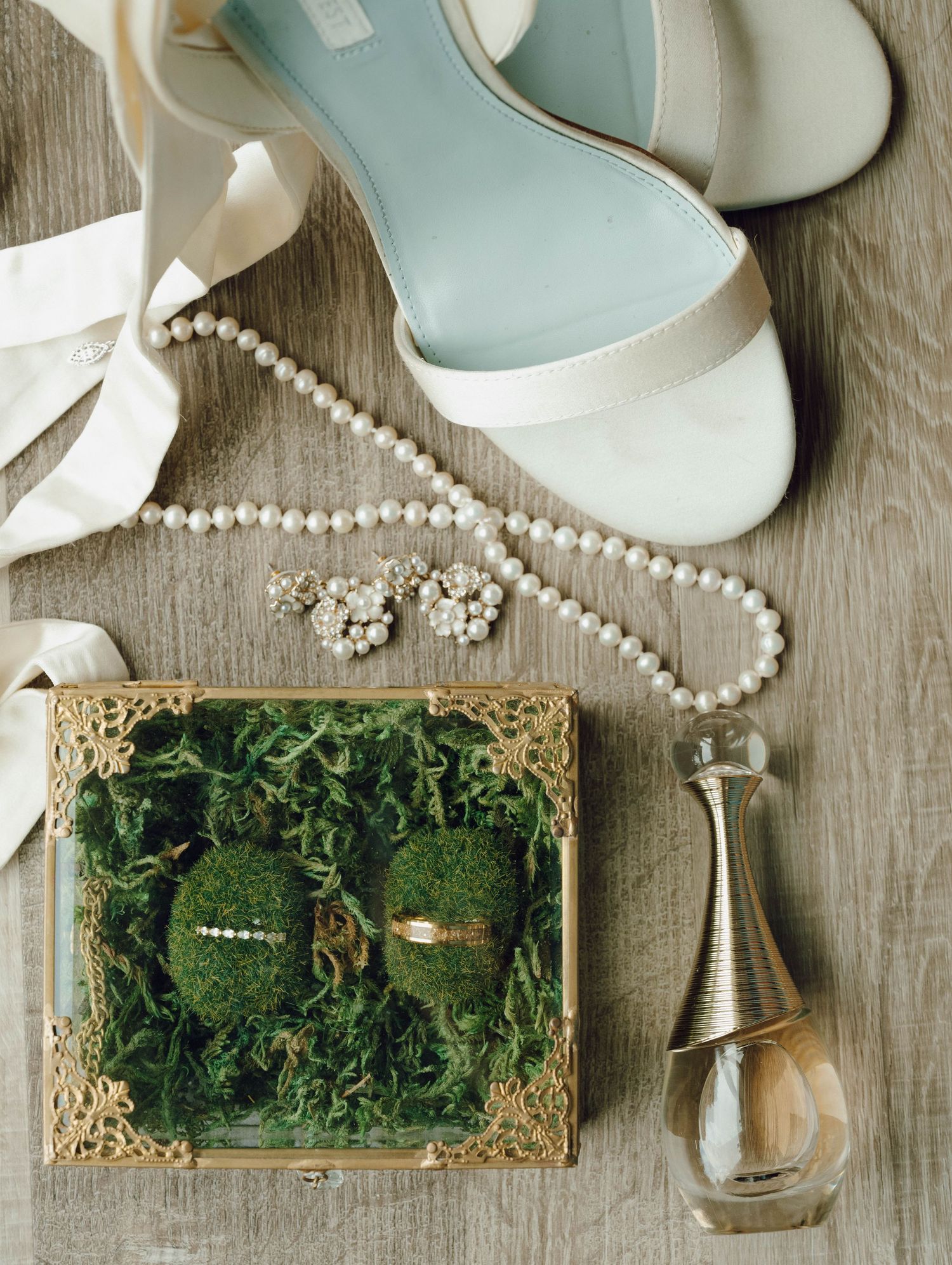 Elegant mint and white bridal shoes with pearl jewelry and moss-filled ring box on wooden surface.
