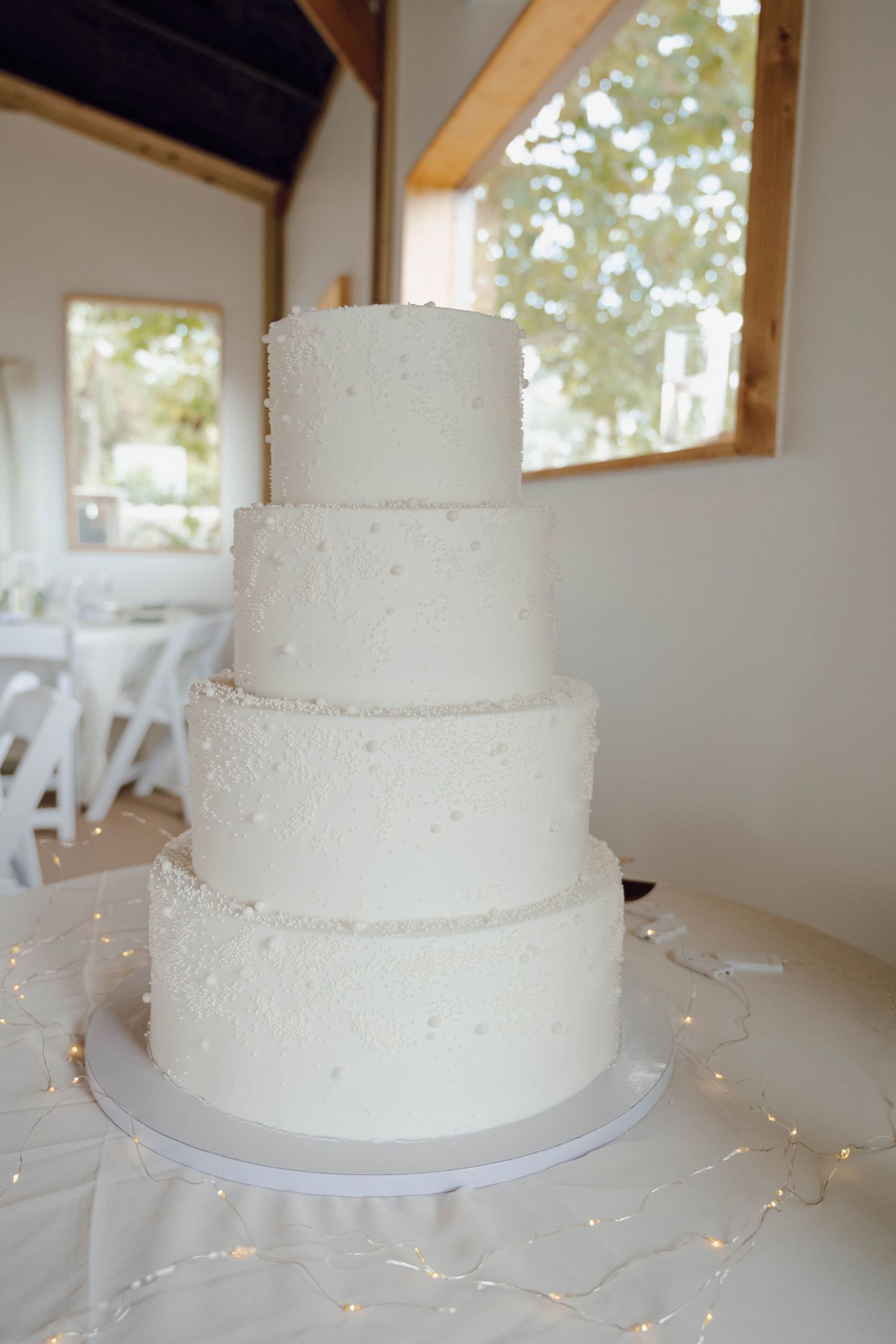 Three-tiered white wedding cake with simple frosting displayed on a table in a bright indoor venue.