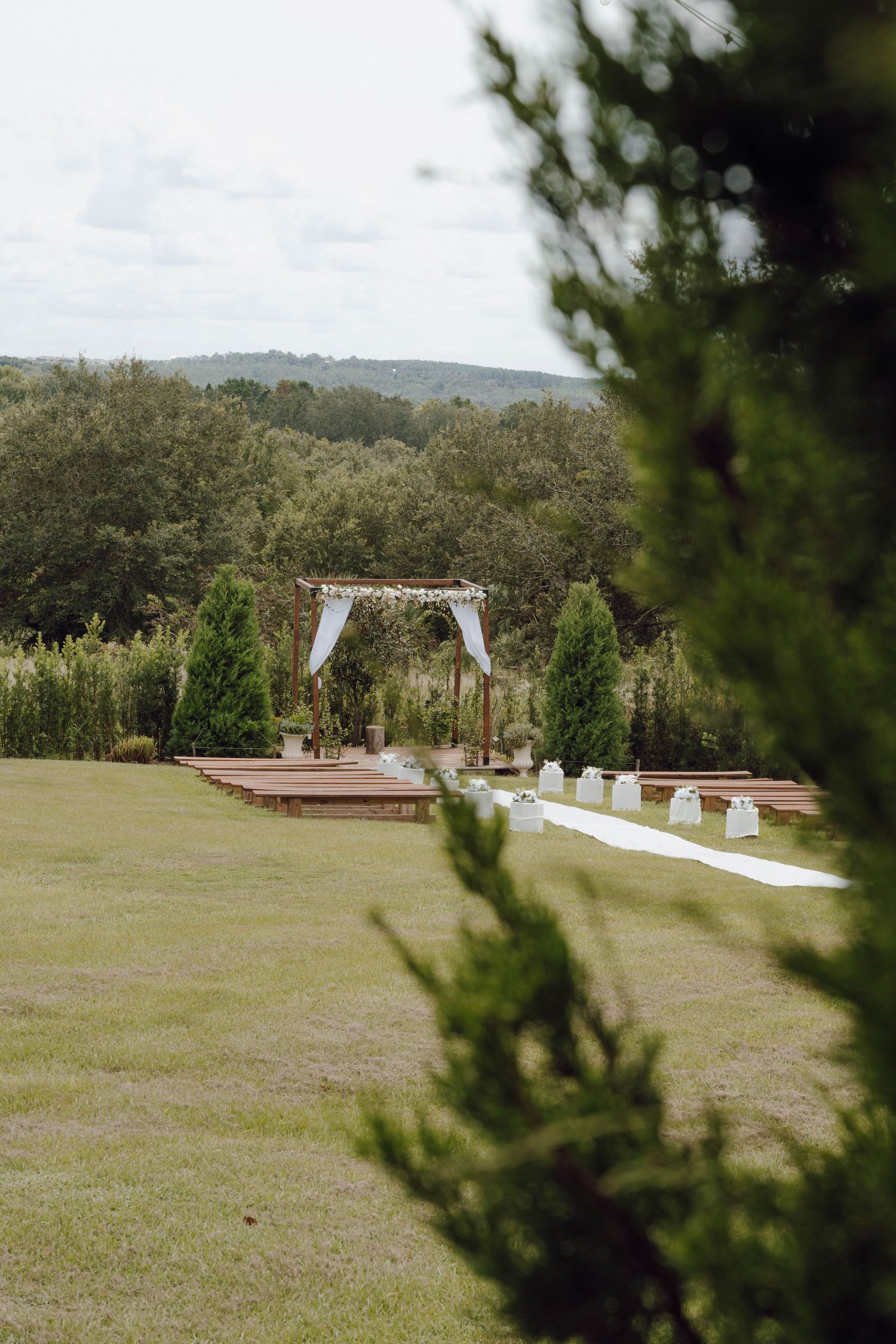 Outdoor wedding ceremony setup with white arch and seating on a grassy hillside overlooking mountain views.