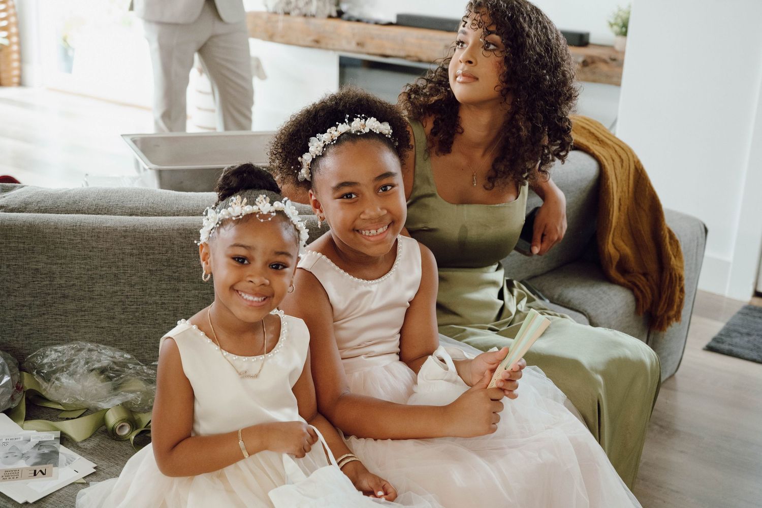 Two young attendants in white dresses with floral headpieces smile together during a wedding celebration.