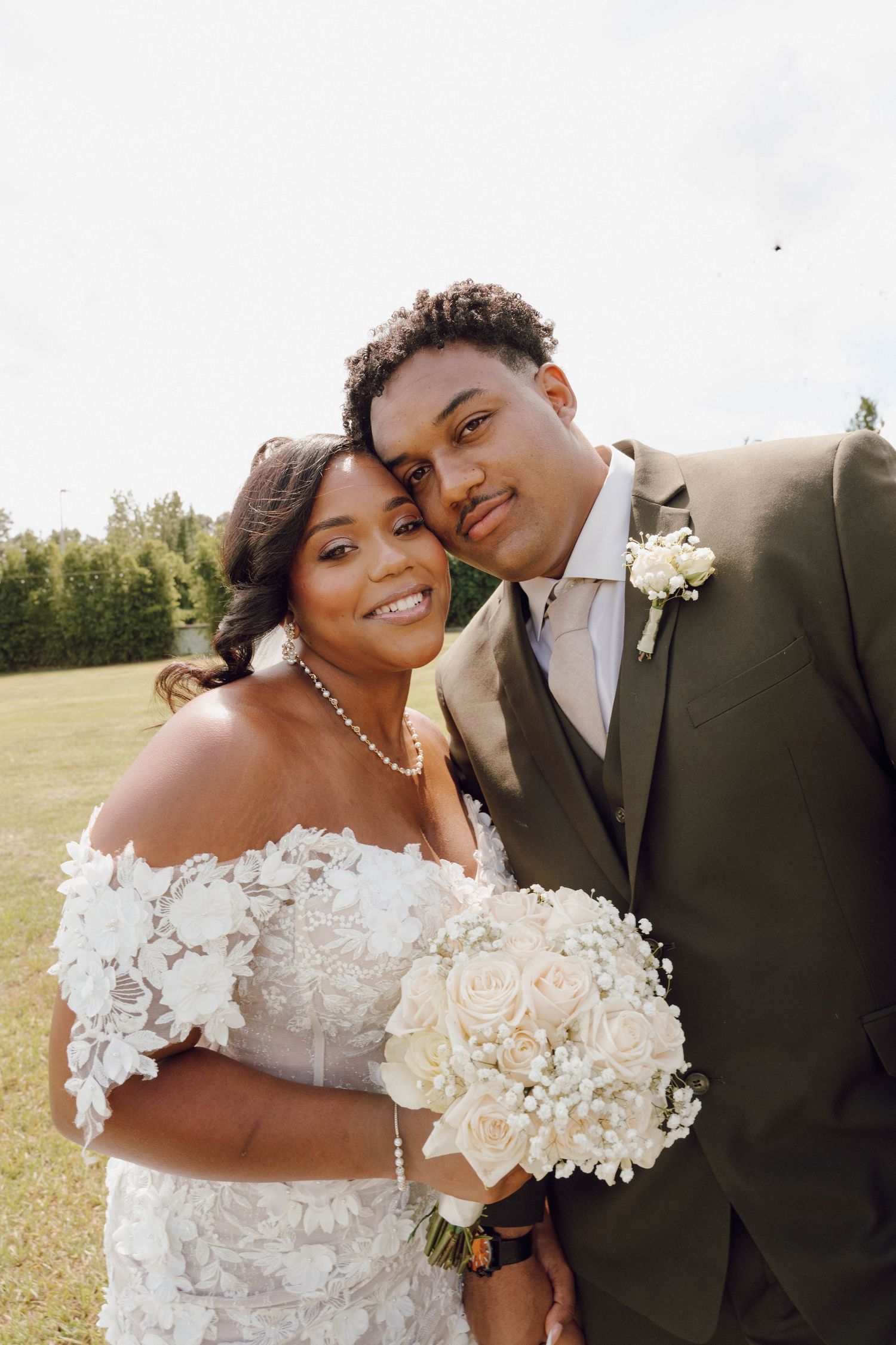 A romantic wedding portrait showing a couple in formal attire with a white bouquet outdoors.