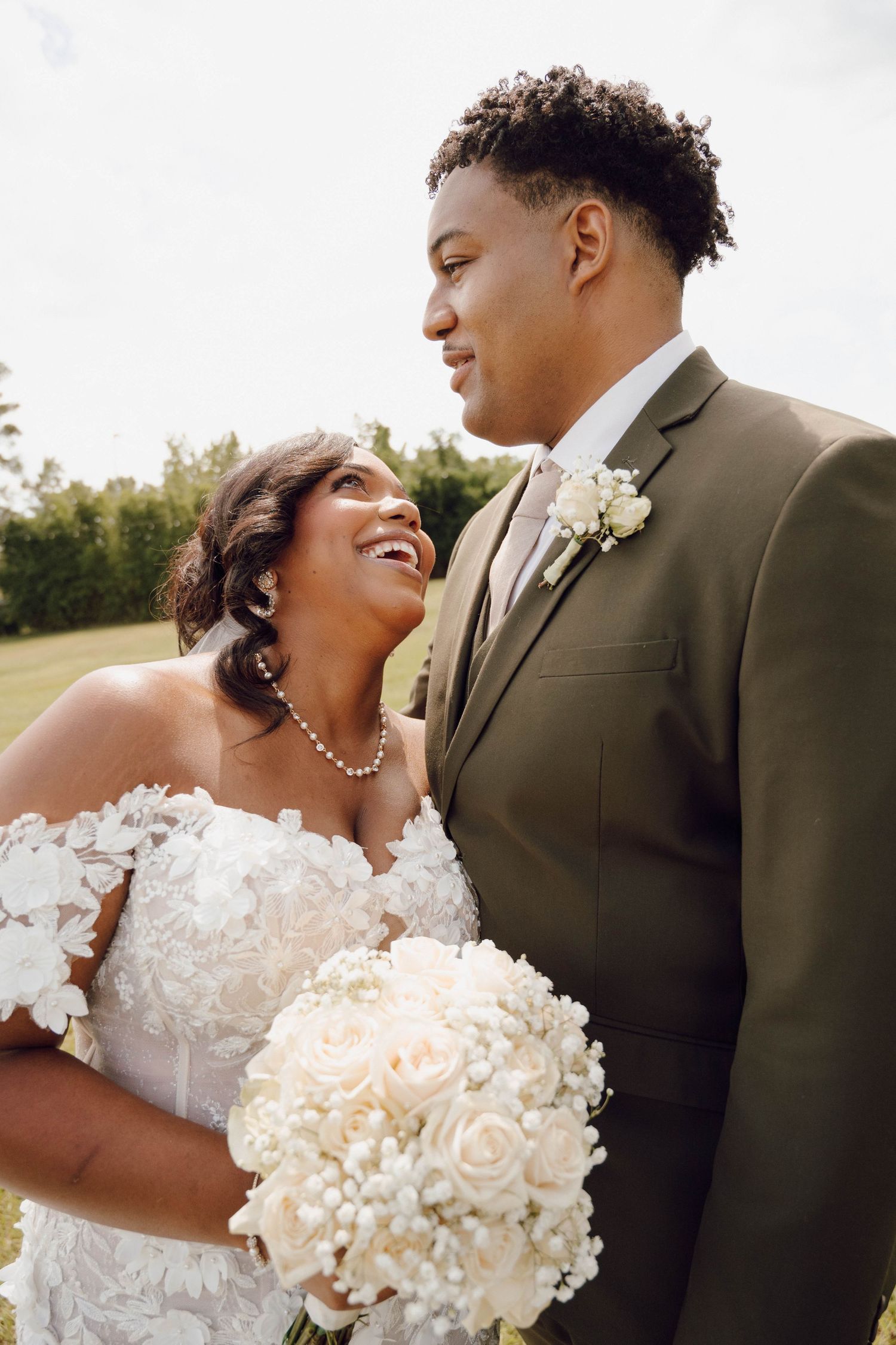 A romantic wedding couple shares intimate moments outdoors while wearing elegant white and olive formal attire.