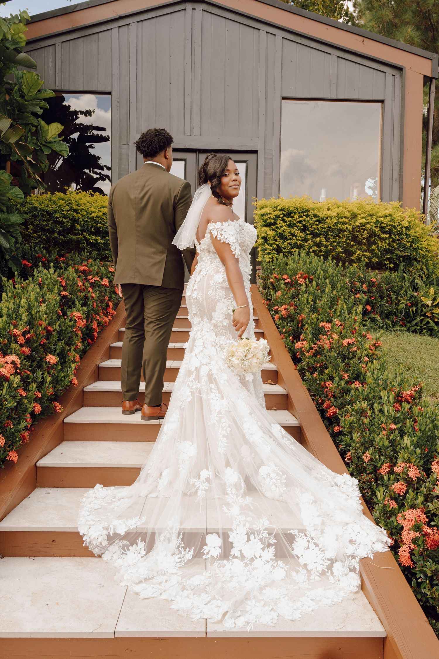 A stunning wedding dress with a long lace train photographed on outdoor steps with blooming flowers.
