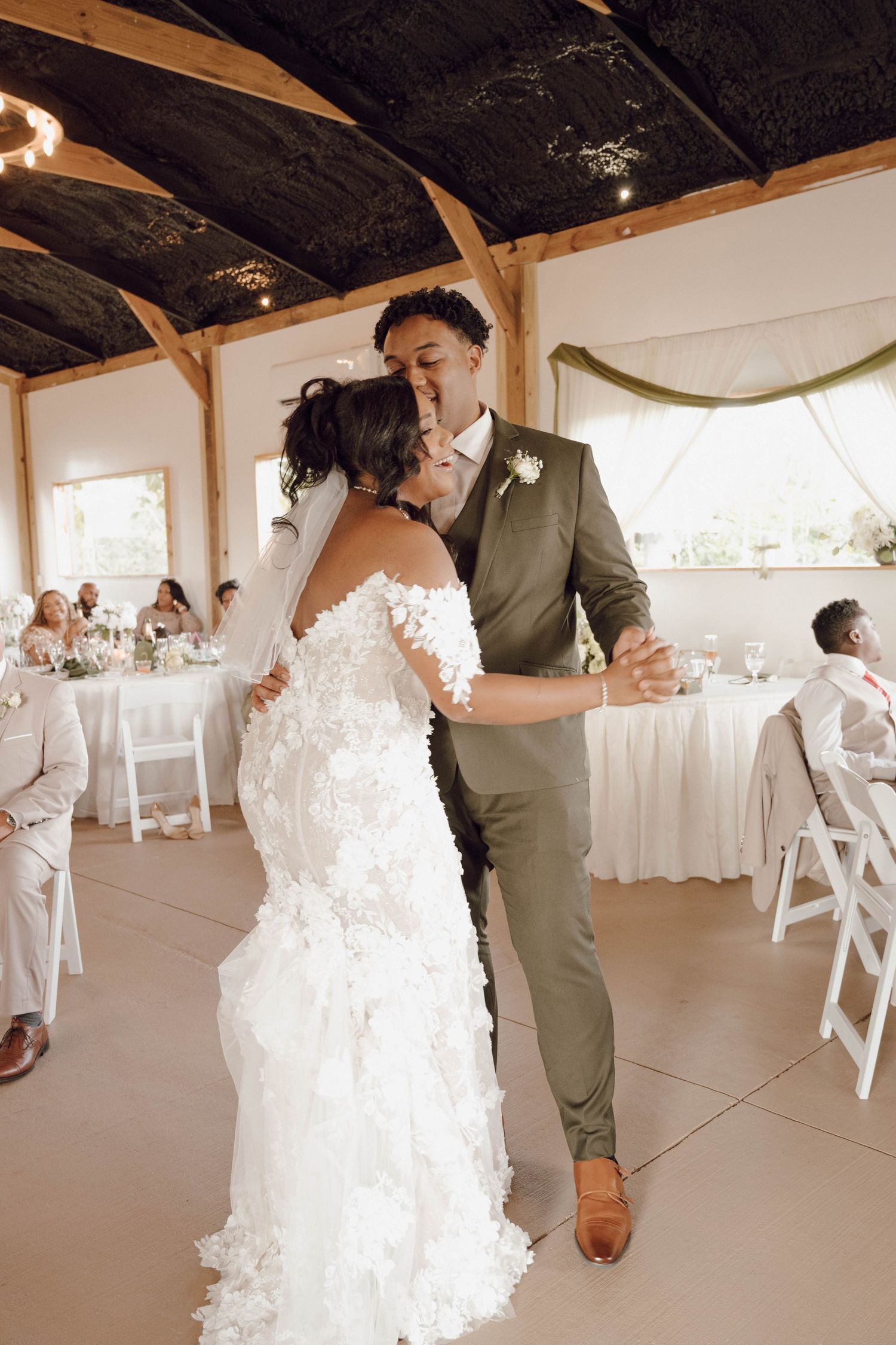 A couple shares their first dance at their wedding reception in an elegant venue with white decor.