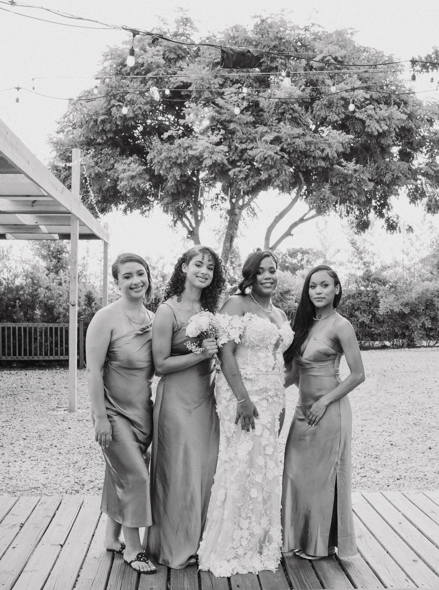 Wedding party in matching sage green dresses poses together on a wooden deck outdoors.