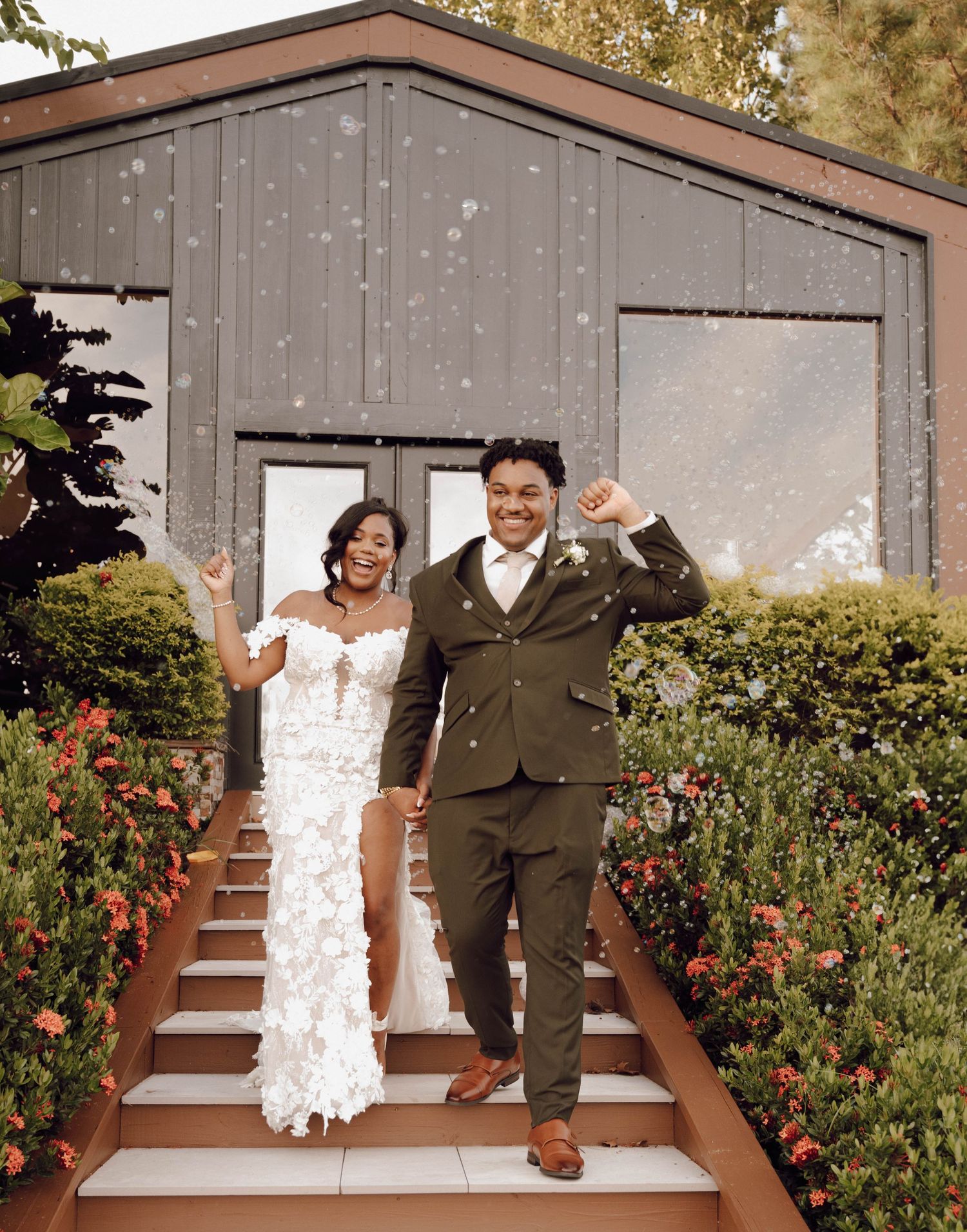 Newlyweds celebrate with excitement on garden steps outside a modern building.