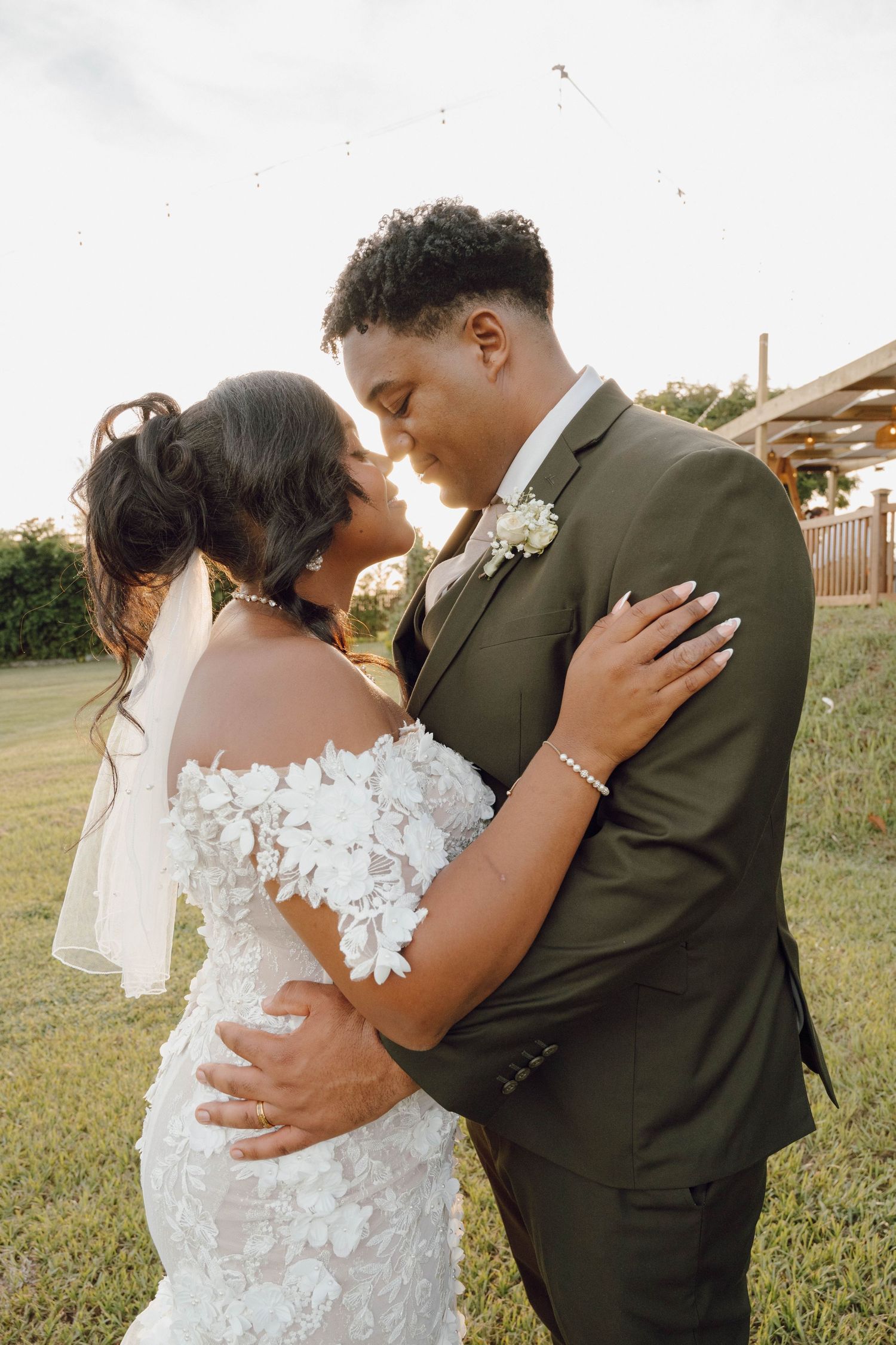 An intimate wedding portrait of a couple embracing outdoors with the bride in lace and groom in olive suit.