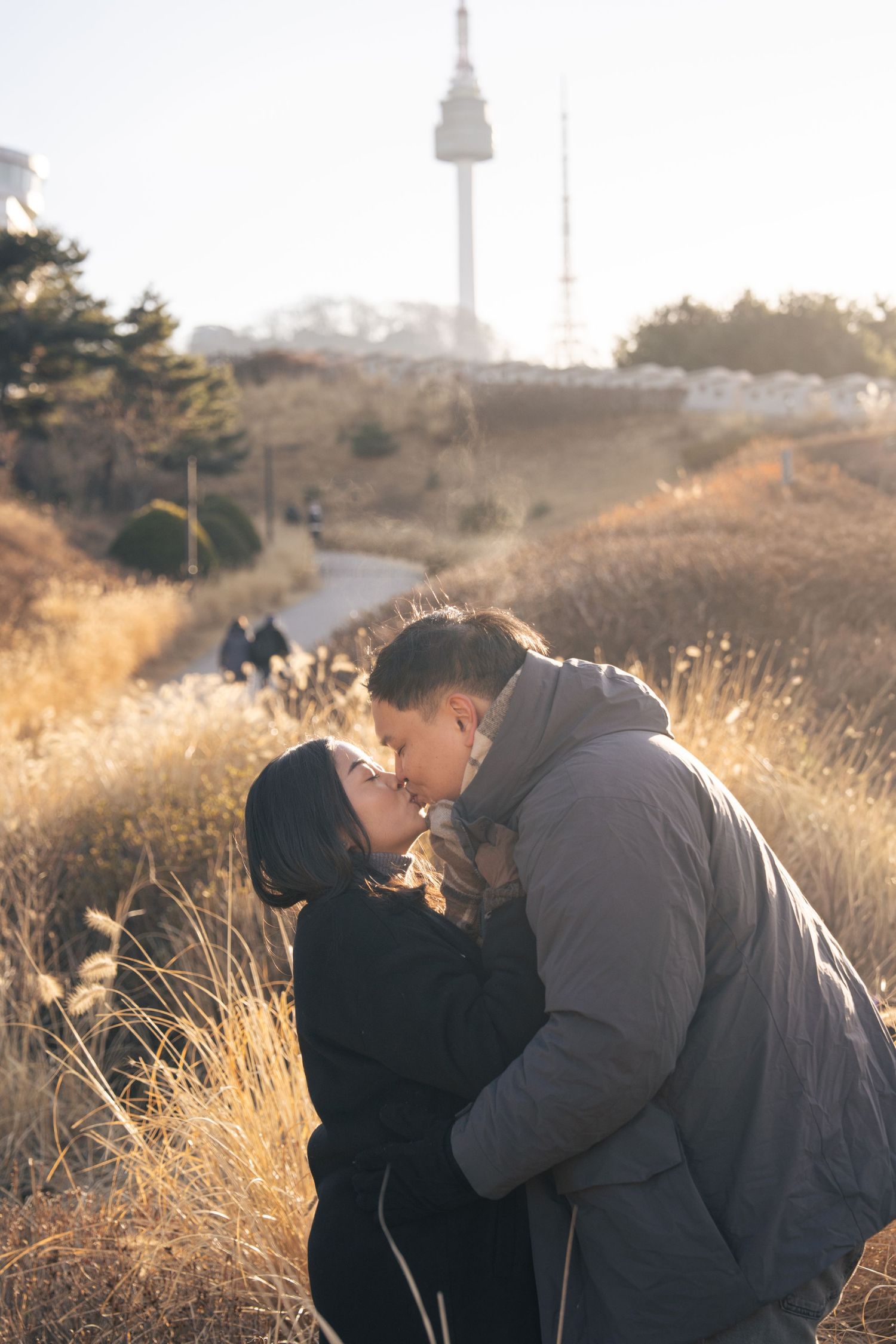 A couple embraces in a romantic moment at sunset on a hillside with golden grass and soft lighting.