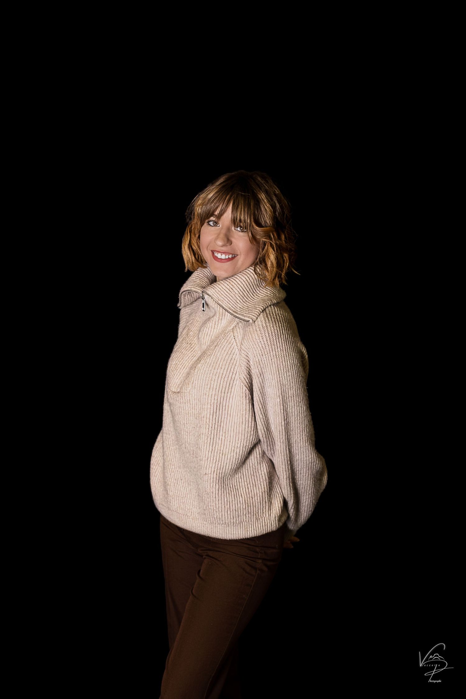 Figure in beige sweater poses dramatically against black background.