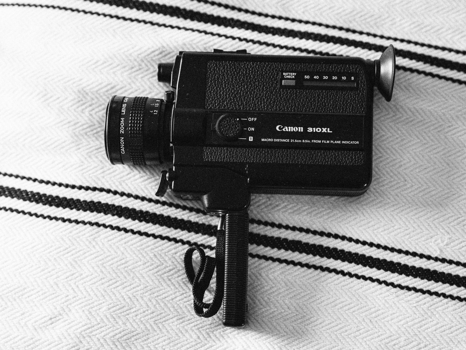 Vintage Canon Super 8 movie camera with black finish displayed on striped fabric background.