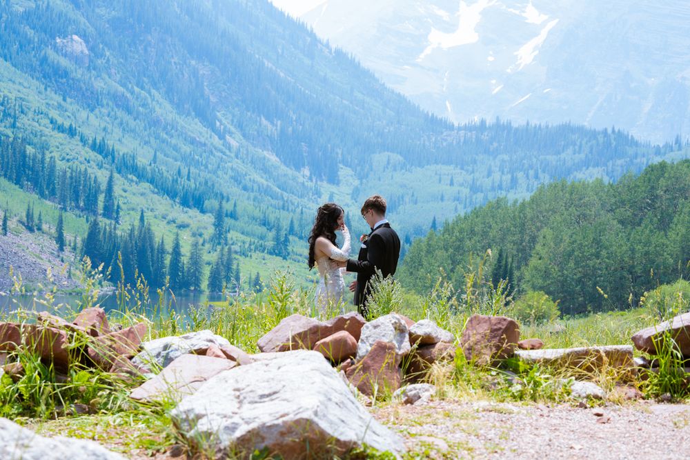 Couple shares a romantic moment on a mountainside surrounded by rocky peaks and green forest.