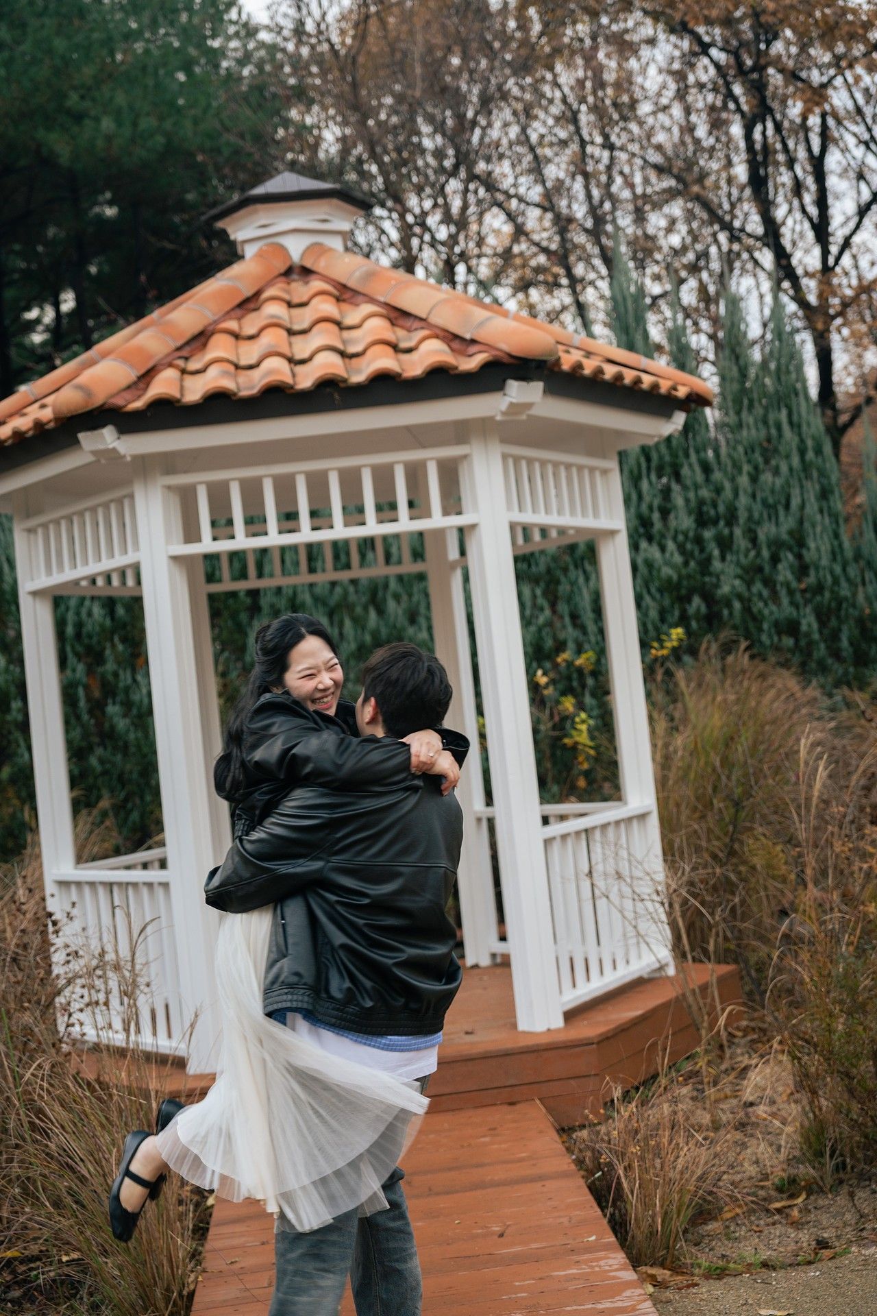 A couple embraces and spins in a romantic moment at a white gazebo surrounded by autumn foliage.