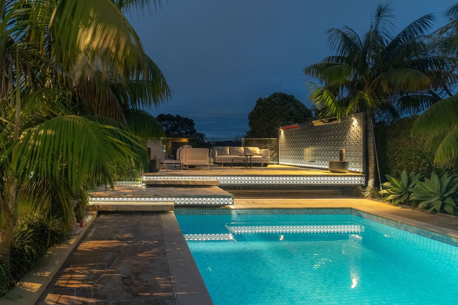 Tropical poolside setting with palm trees and modern lighting at twilight.