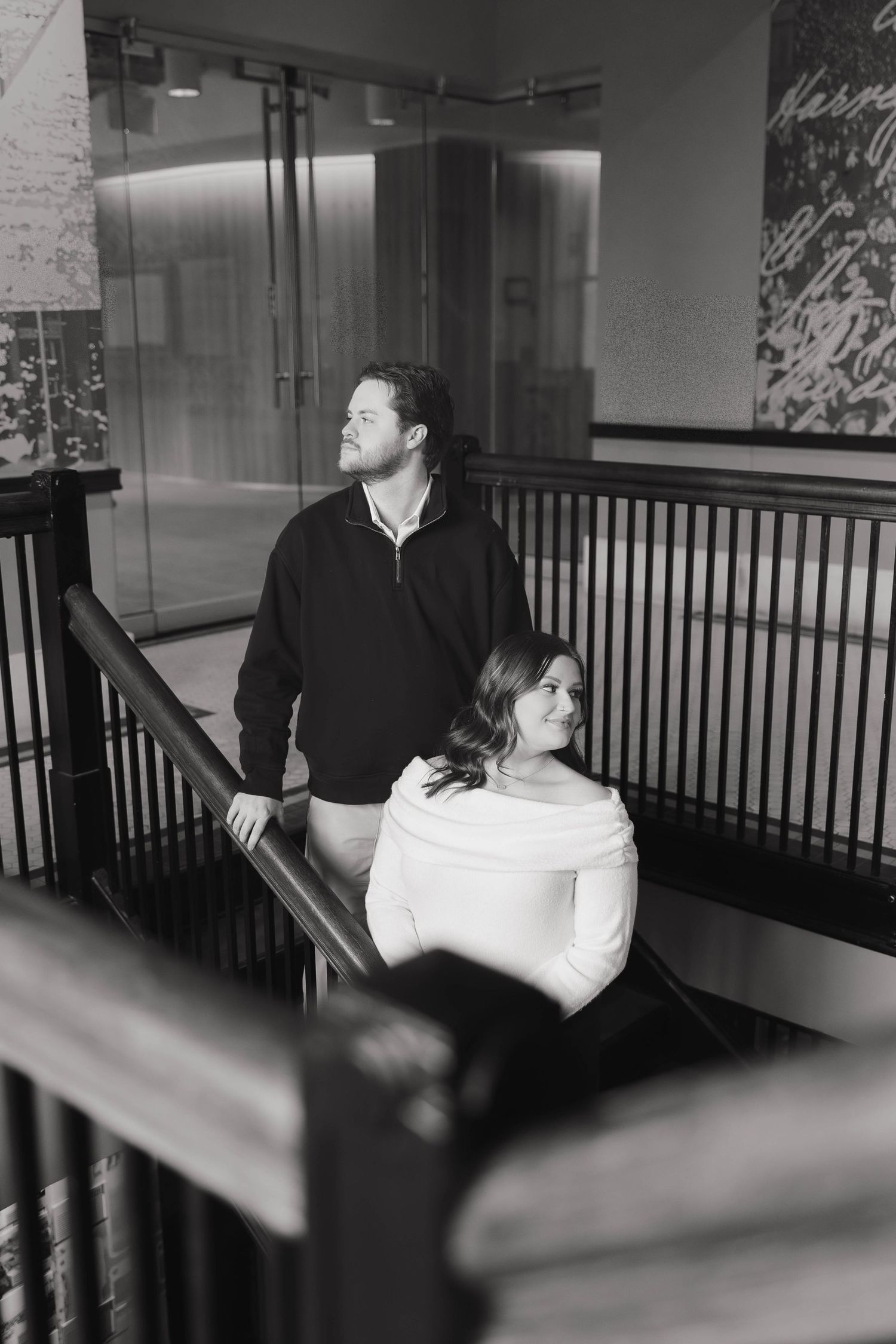 Black and white photograph showing a couple in a dimly lit interior space with railings visible.