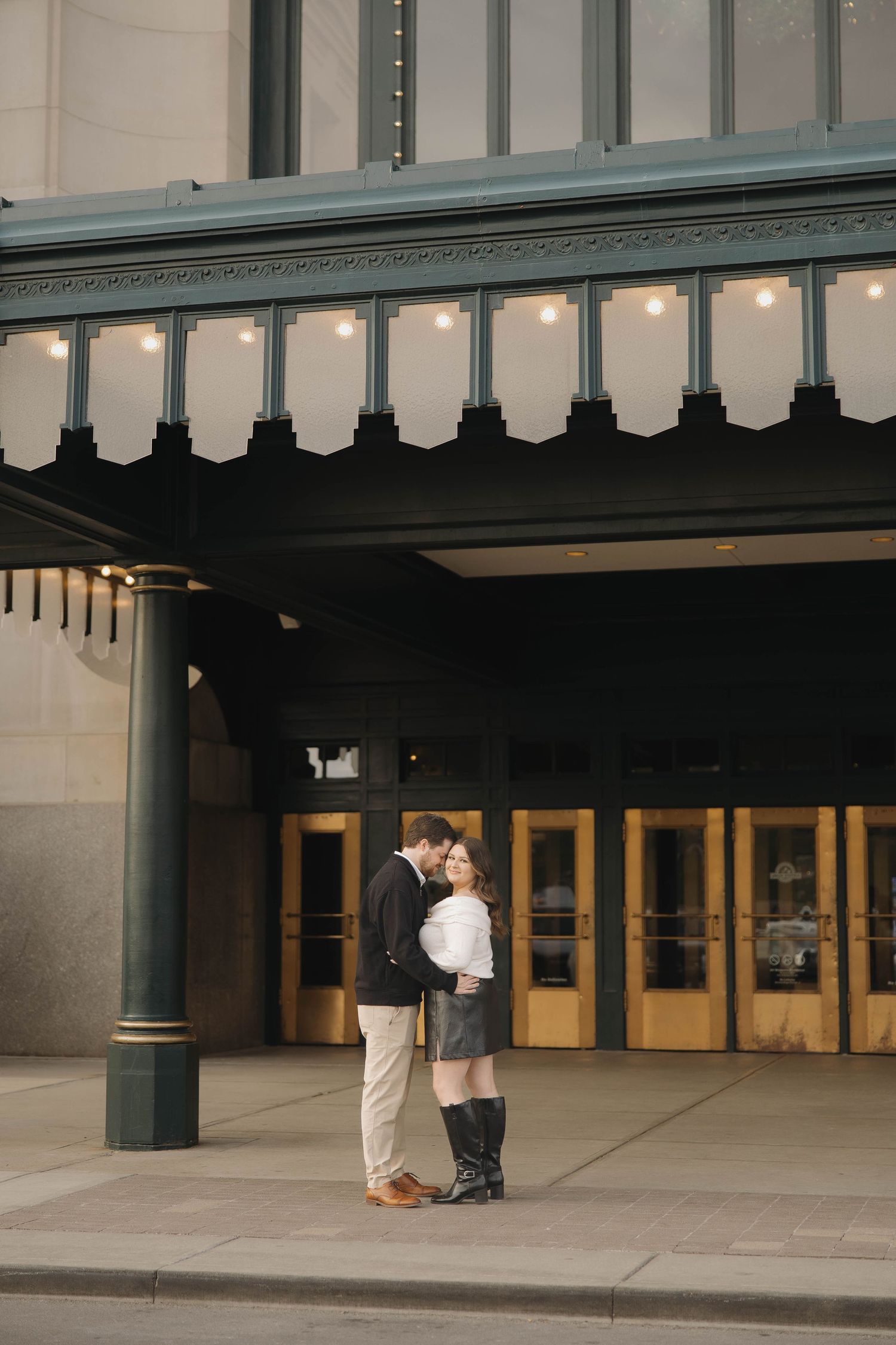 A couple shares an intimate moment under a covered walkway with elegant columns and archways.