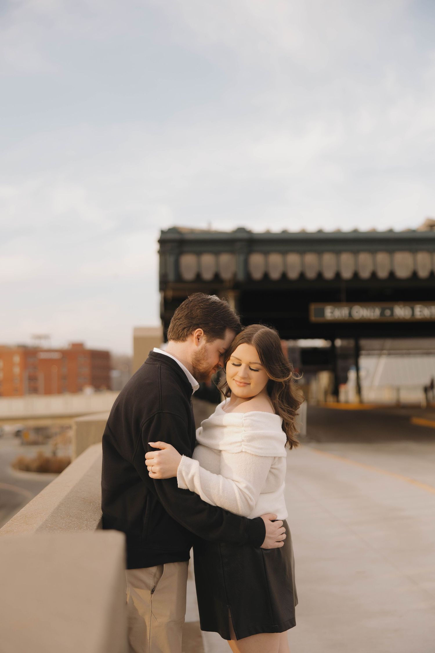A romantic couple embraces in front of an industrial building during golden hour.