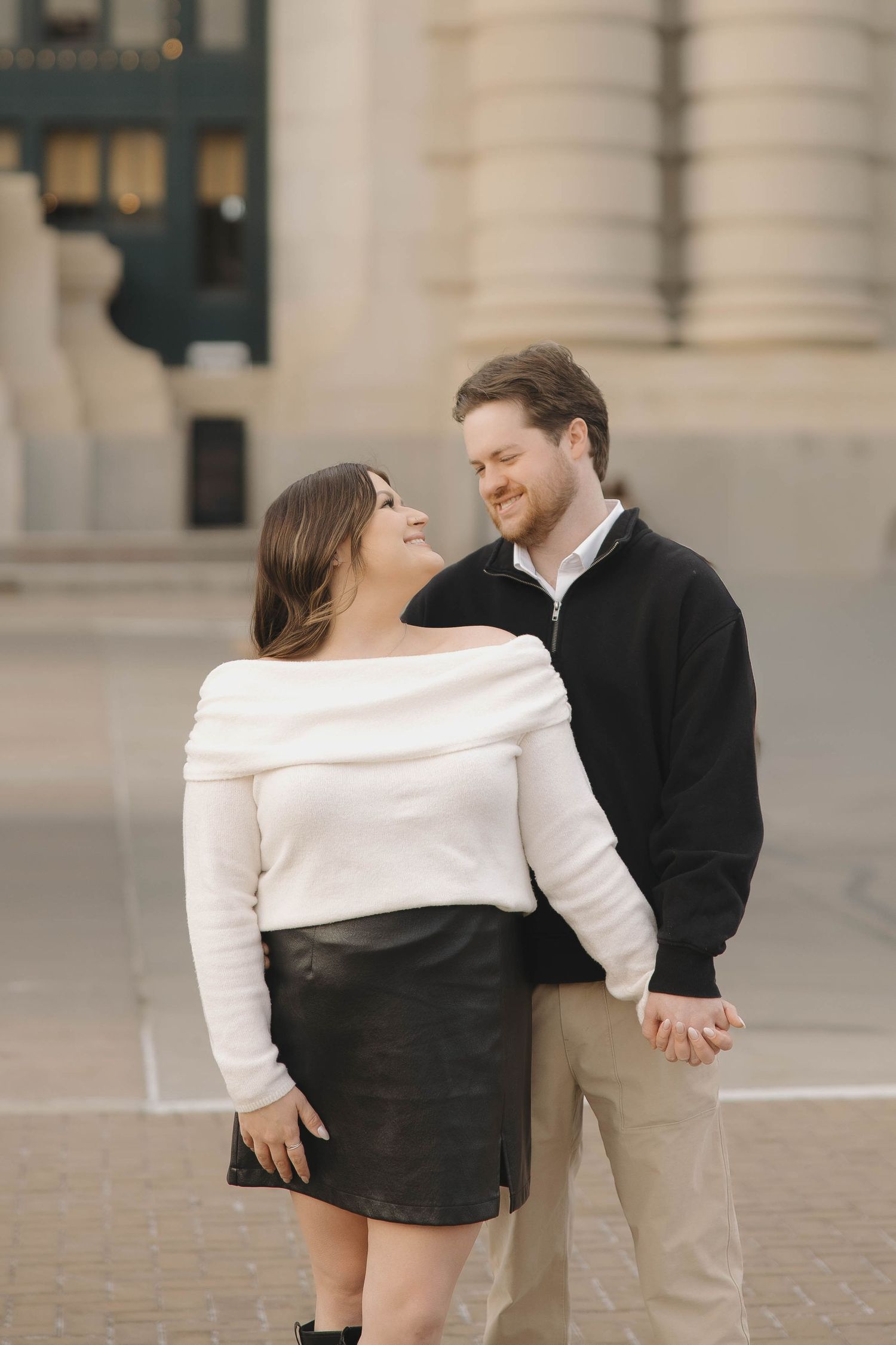 A couple in formal attire dances together gracefully on a stone paved courtyard with elegant architecture in the background.