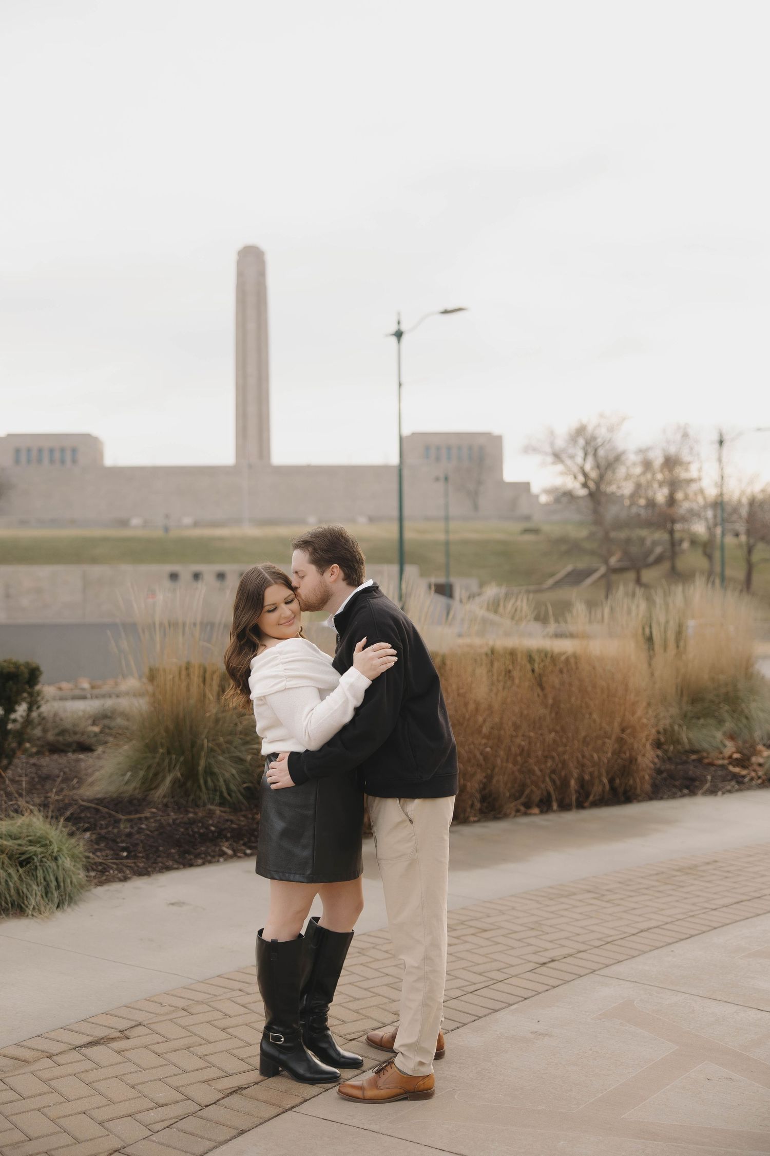 A couple sharing an intimate moment on a brick pathway with industrial buildings in the misty background.